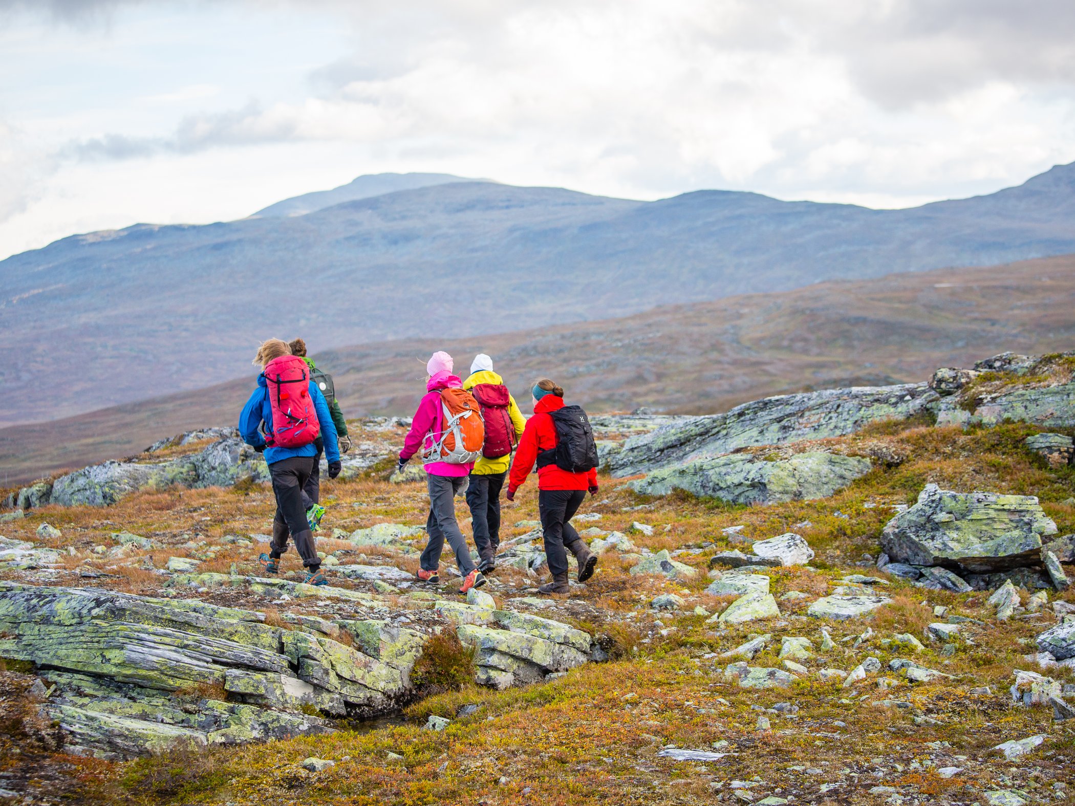 Grupp vandrare går över stenig fjällhed i öppet fjällandskap.