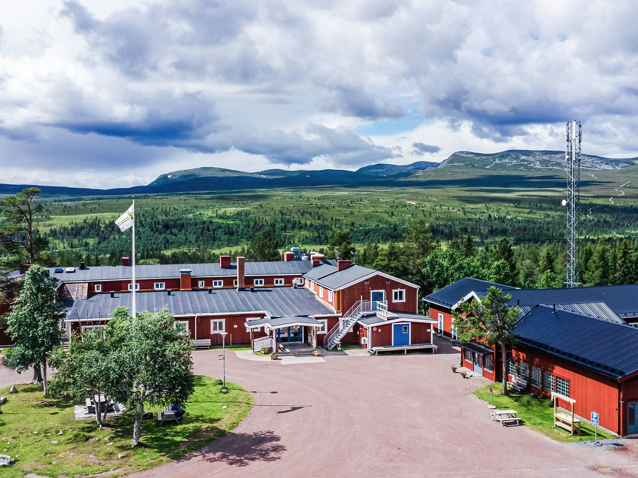 Fjällstation med röda byggnader och utsikt över vidsträckt fjällandskap under en dramatisk molnhimmel.