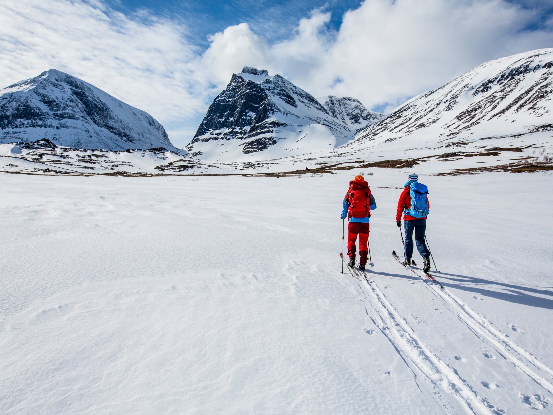 Två personer som åker turskidor mot Kebnekaises fjällmassiv.