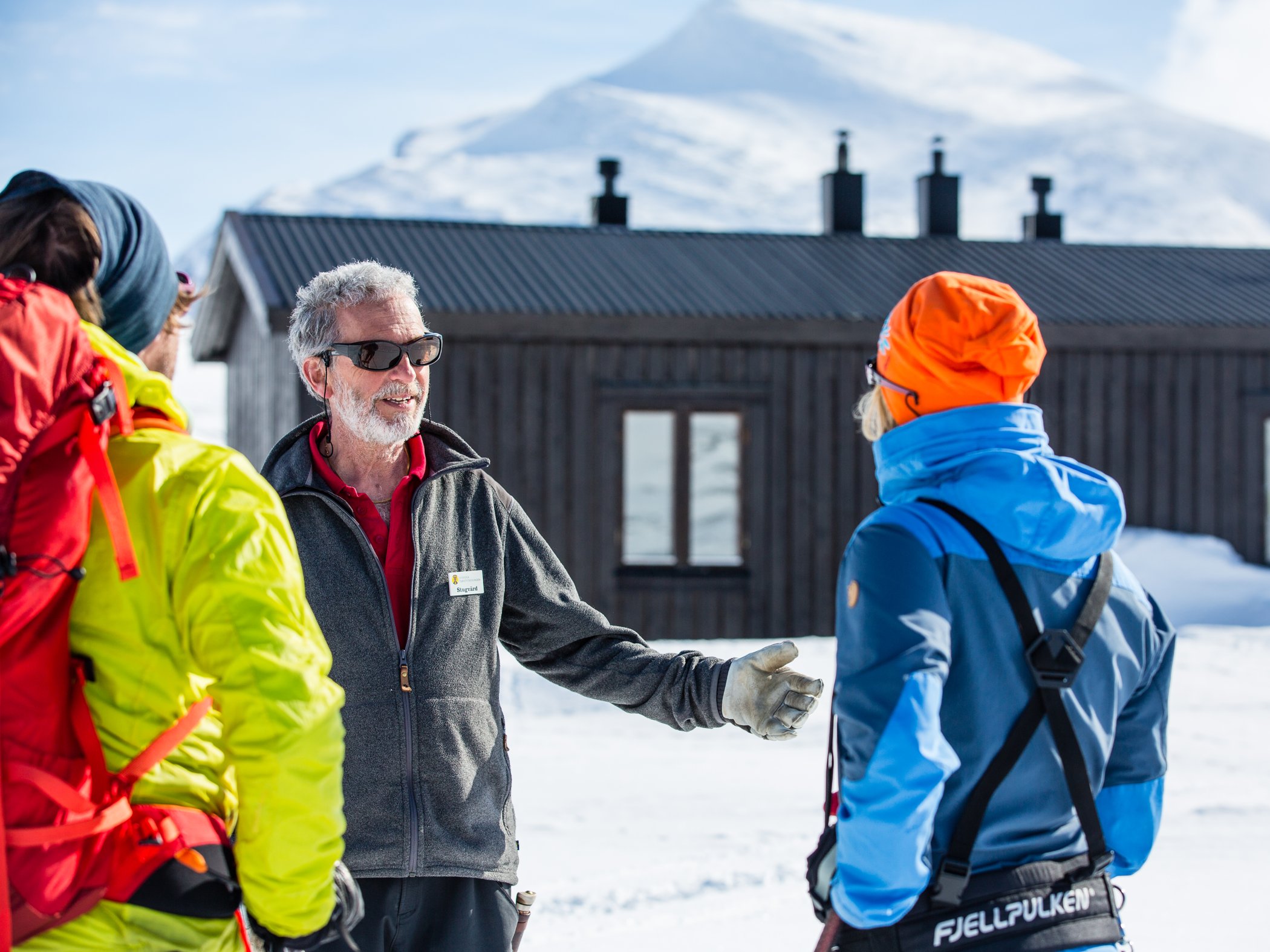 En stugvärd vid fjällstuga som hälsar två personer välkomna en vinterdag. 