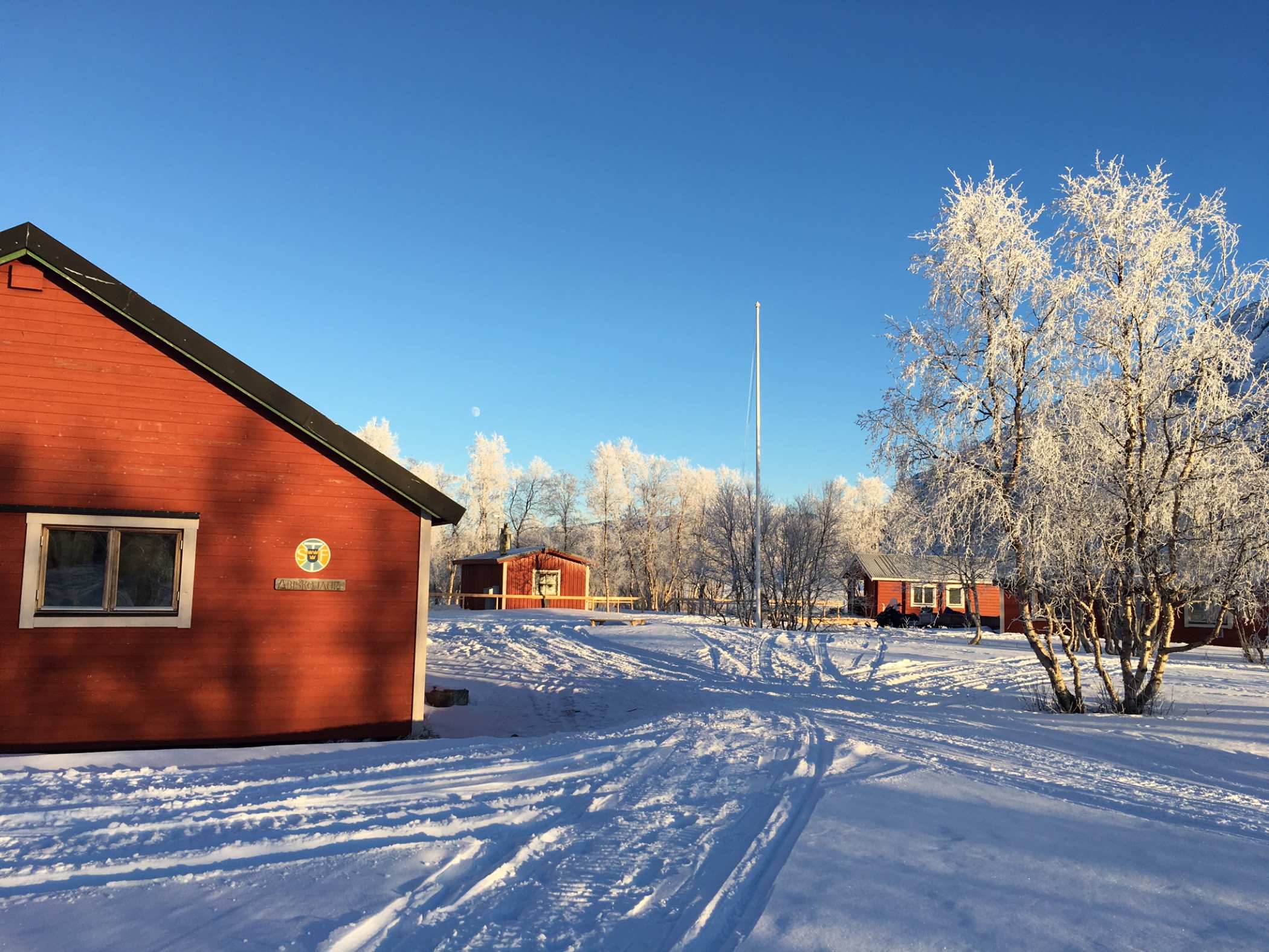 Röda stugor och snötäckta träd vid STF Abiskojaure under klar vinterdag.