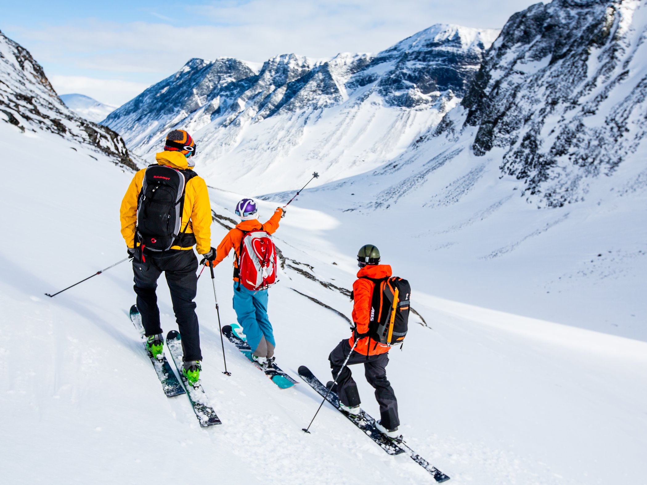 Tre personer med topptursskidor stannar i snotackt hogfjallsterrang och blickar ut over fjalldal.