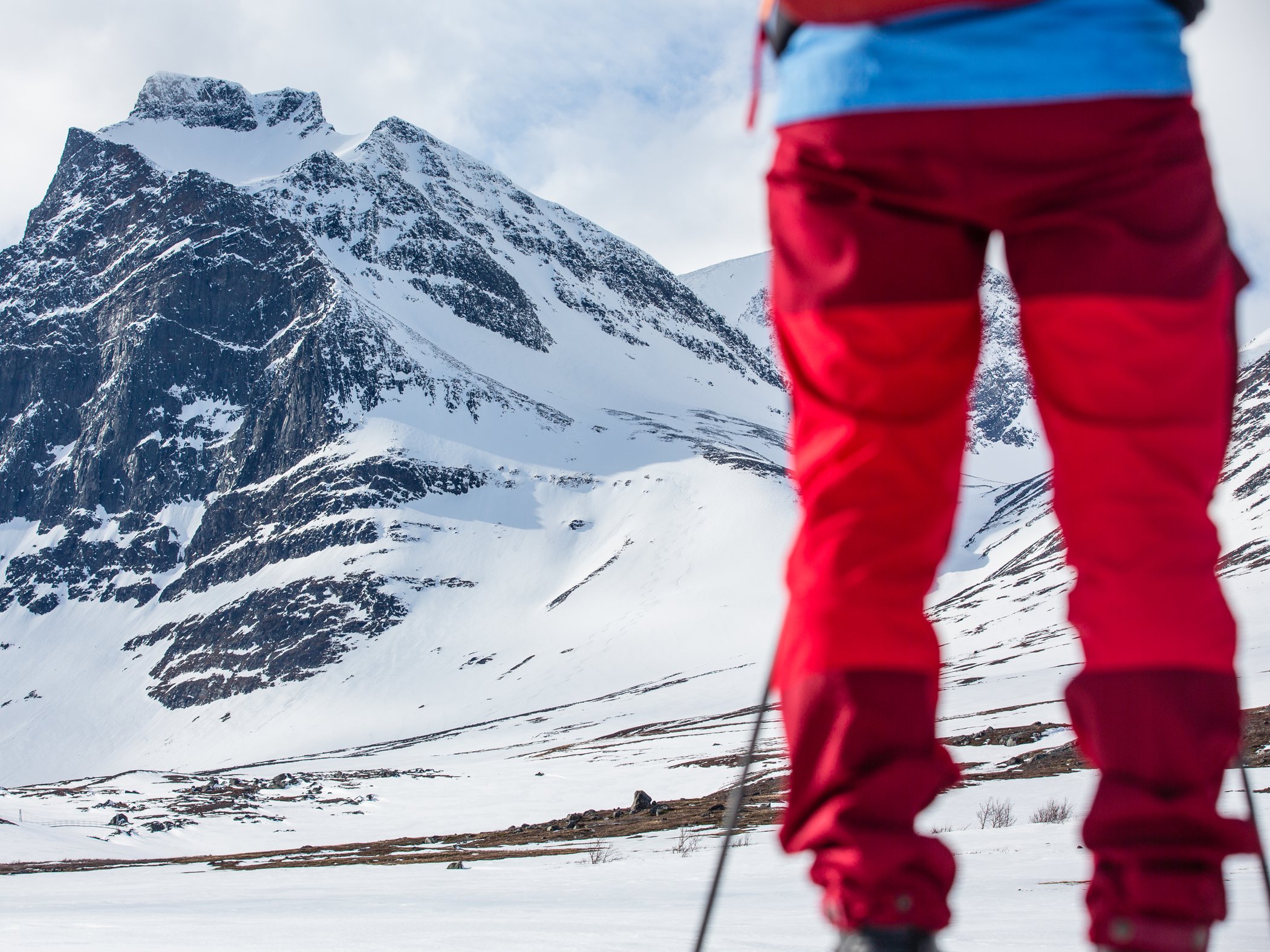 Person med skidor star framfor hoga och snotackta fjall i vinterlandskap.