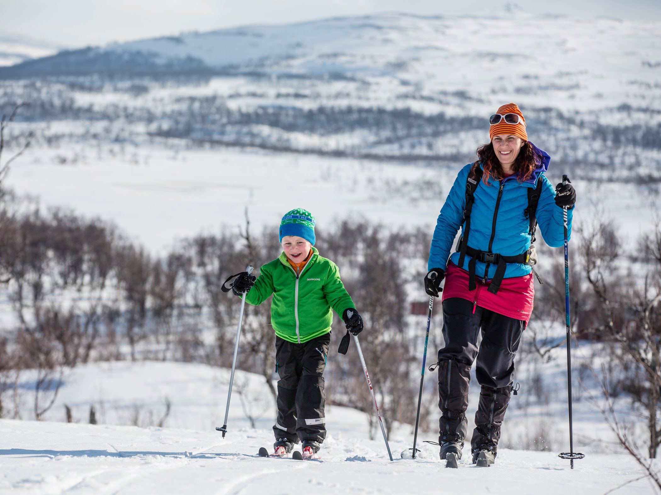 En mamma ohc ett barn som åker skidor ute på ett fjäll.