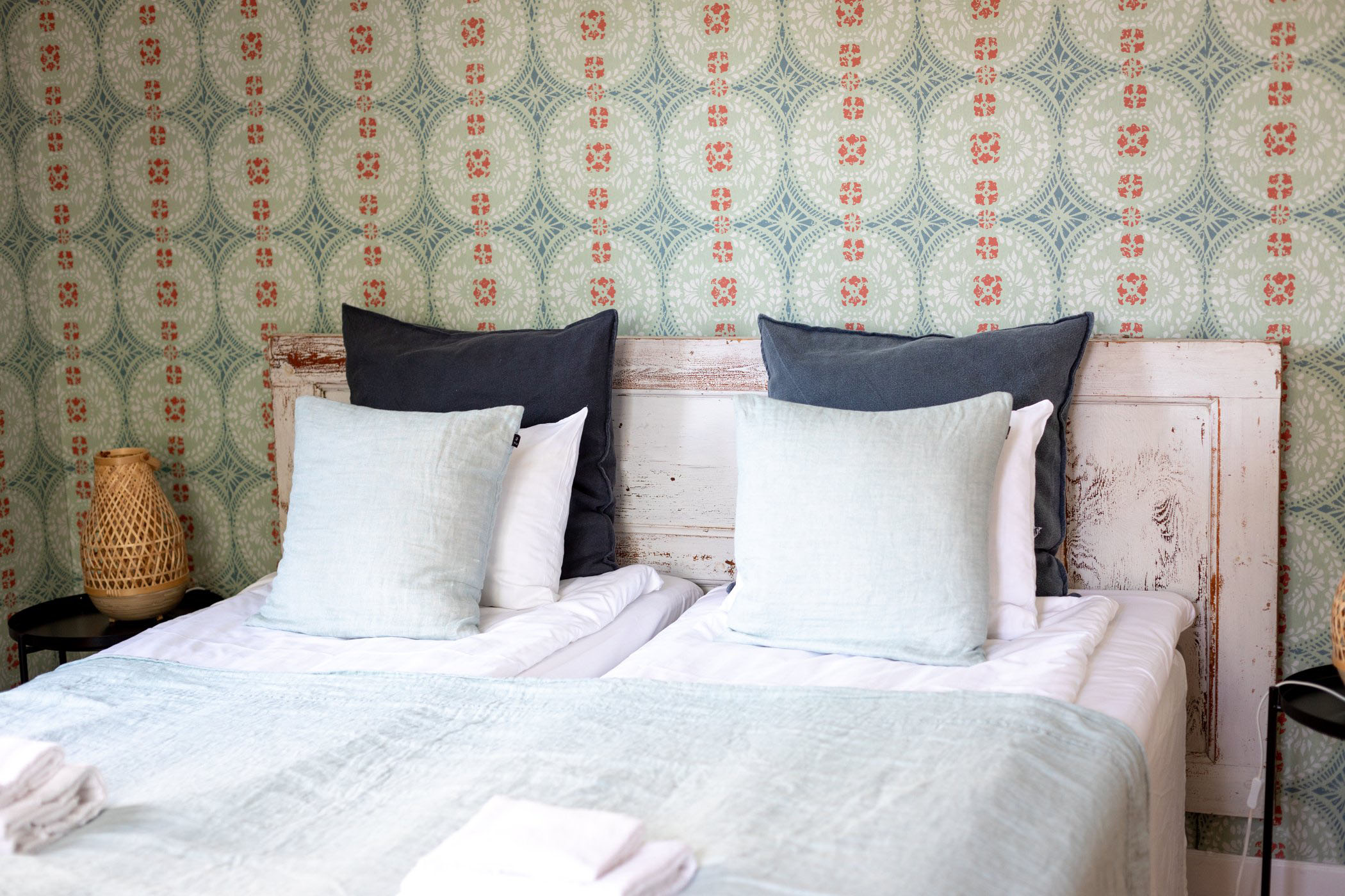 Dubbelrum med två bäddar, ljusa textilier och mönstrad tapet.