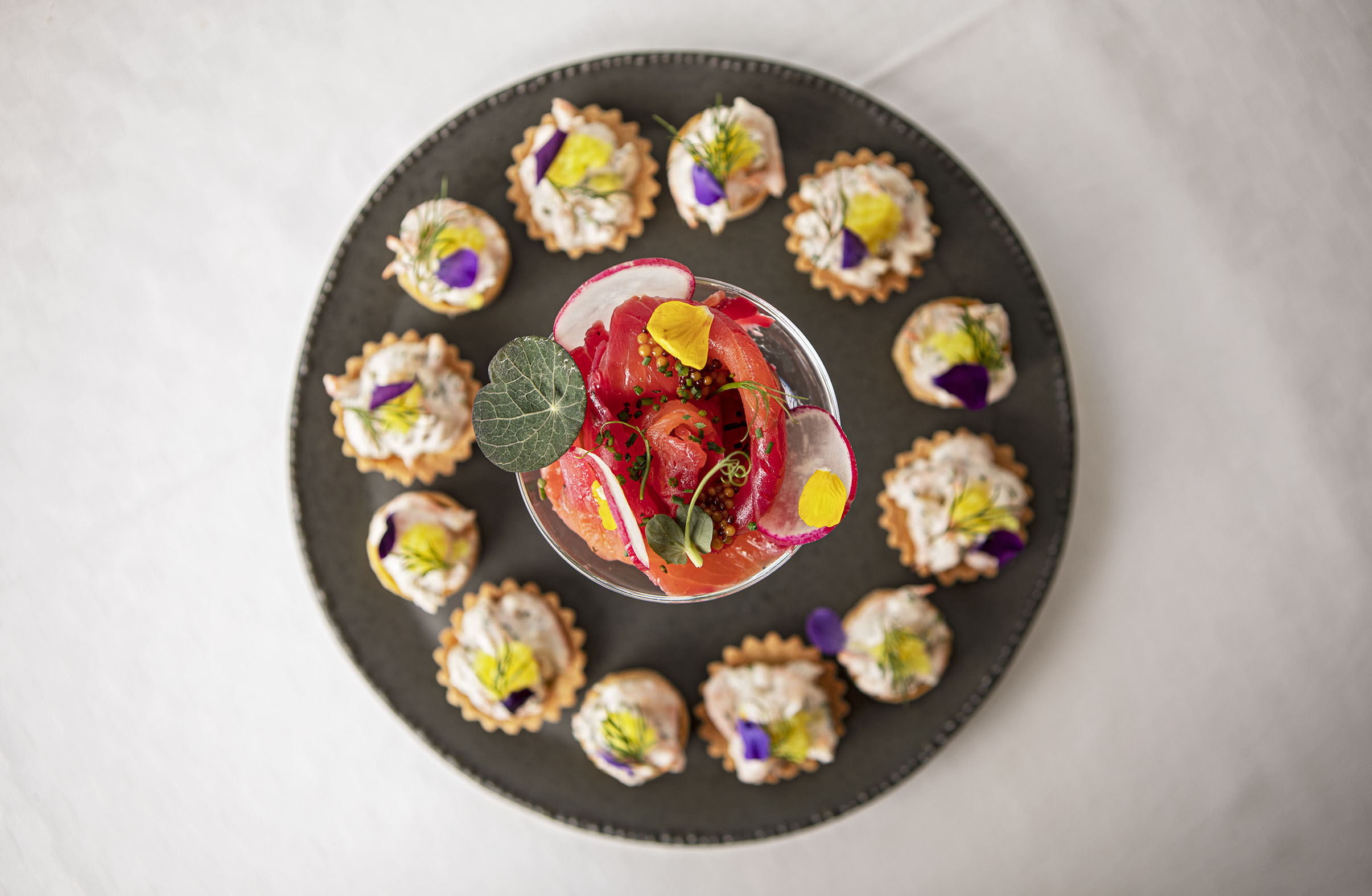 Servering av små aptitretare och lax med garnityr på en tallrik.