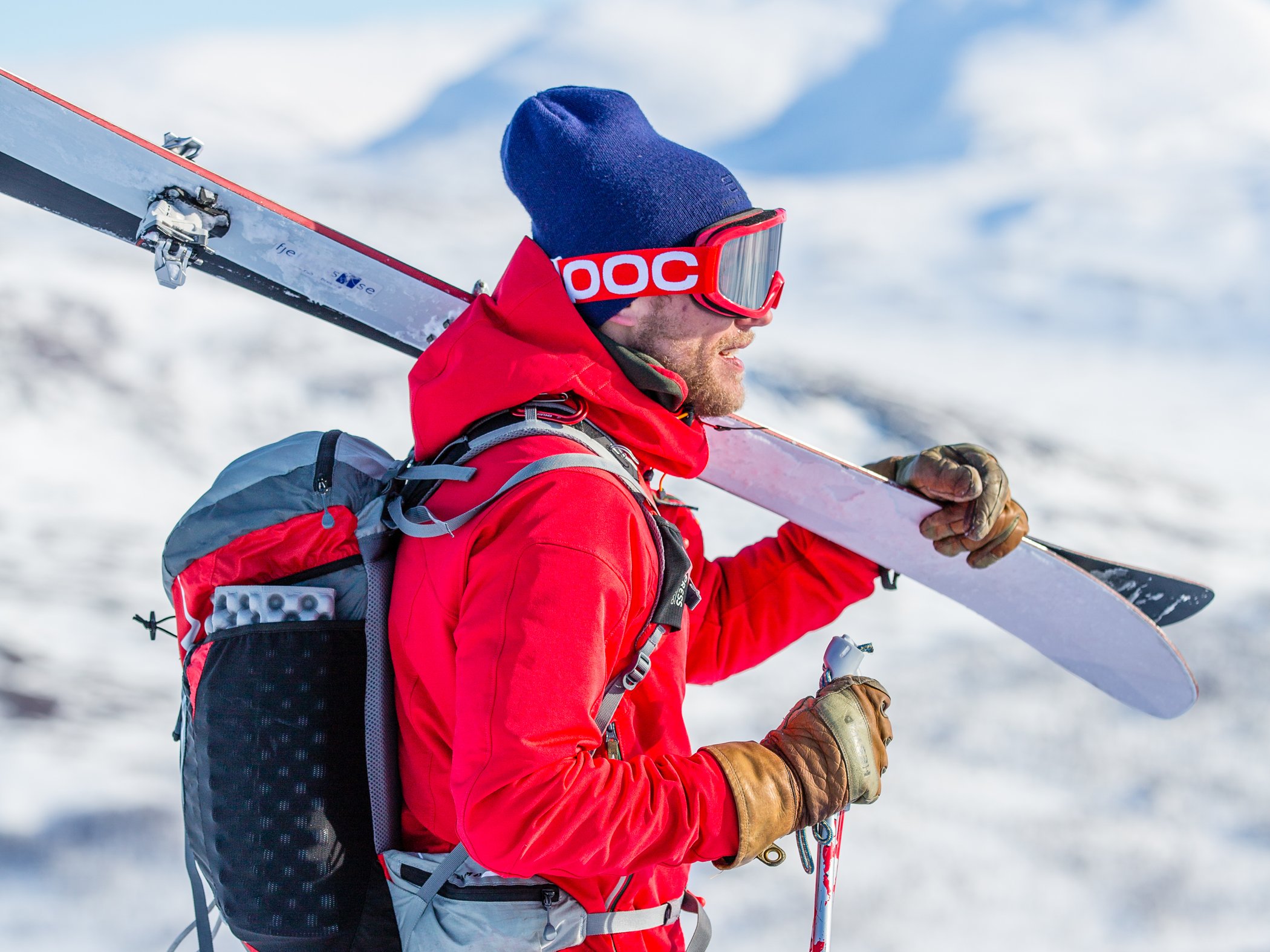 En man i röda skidkläder och röda skidglasögon som bär skidor.