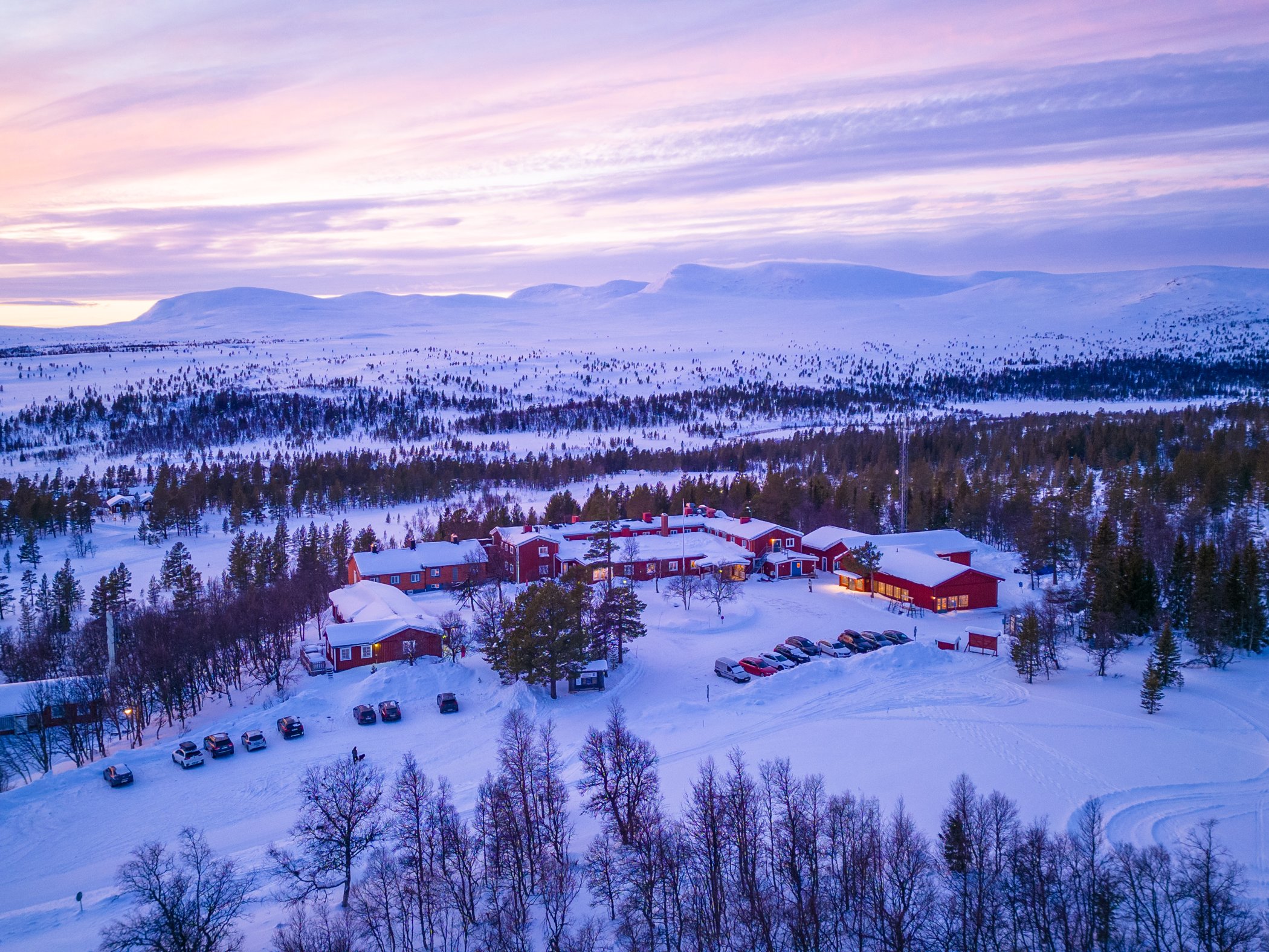 Flygfoto i kvällsljus över Grövelsjöns fjällstation i vinterskrud.