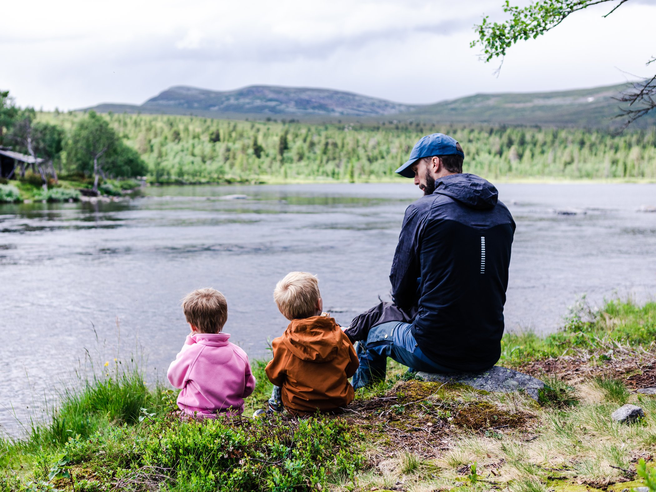 Vuxen och två barn sitter vid en sjö nära Grövelsjön.