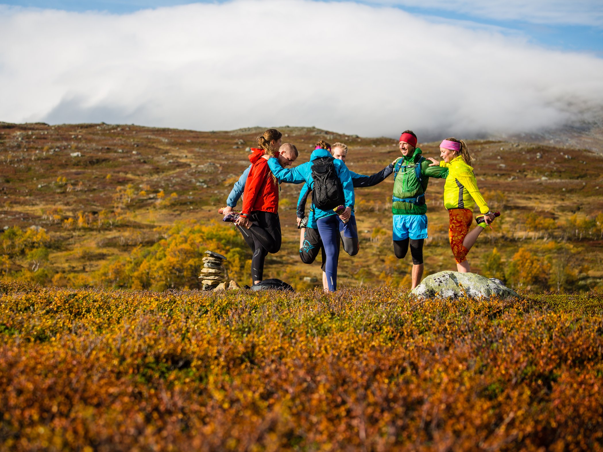 Grupp som stretchar och värmer upp i öppet fjällandskap.