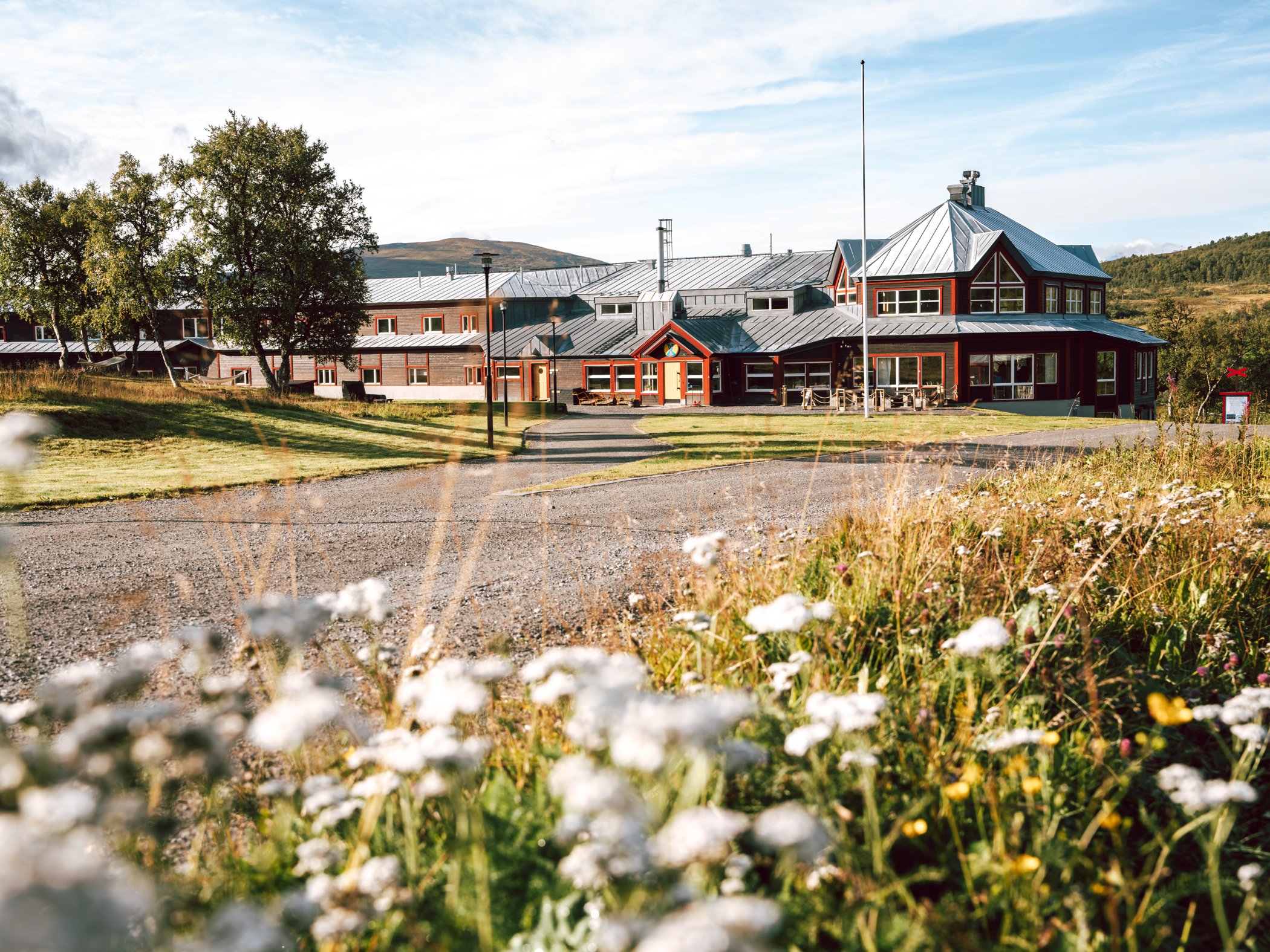 STF Storulvån Fjällstation omgiven av sommaräng och fjällandskap.