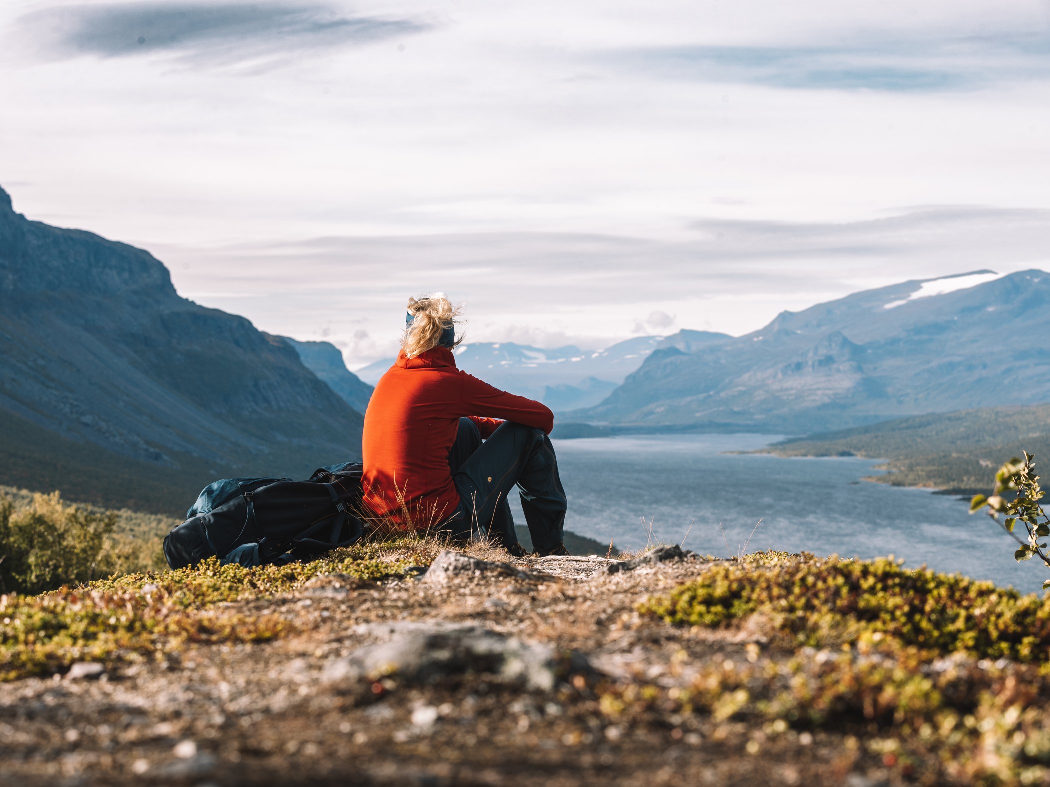 Vandrare sitter och vilar med utsikt över fjällsjö och dalgång.
