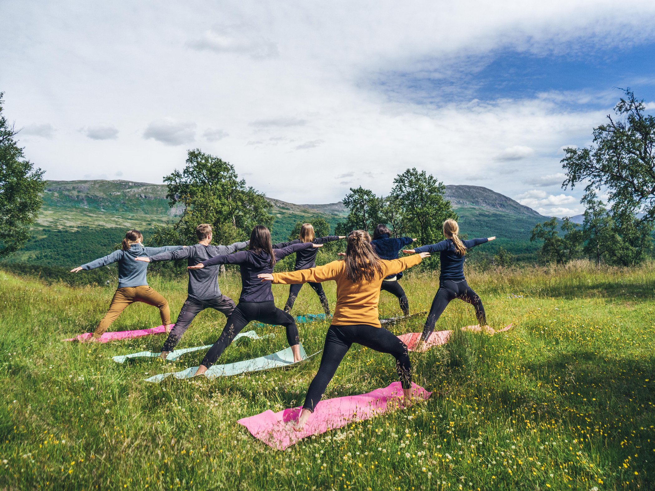 Grupp gör yoga på fjälläng med utsikt över fjällandskap.