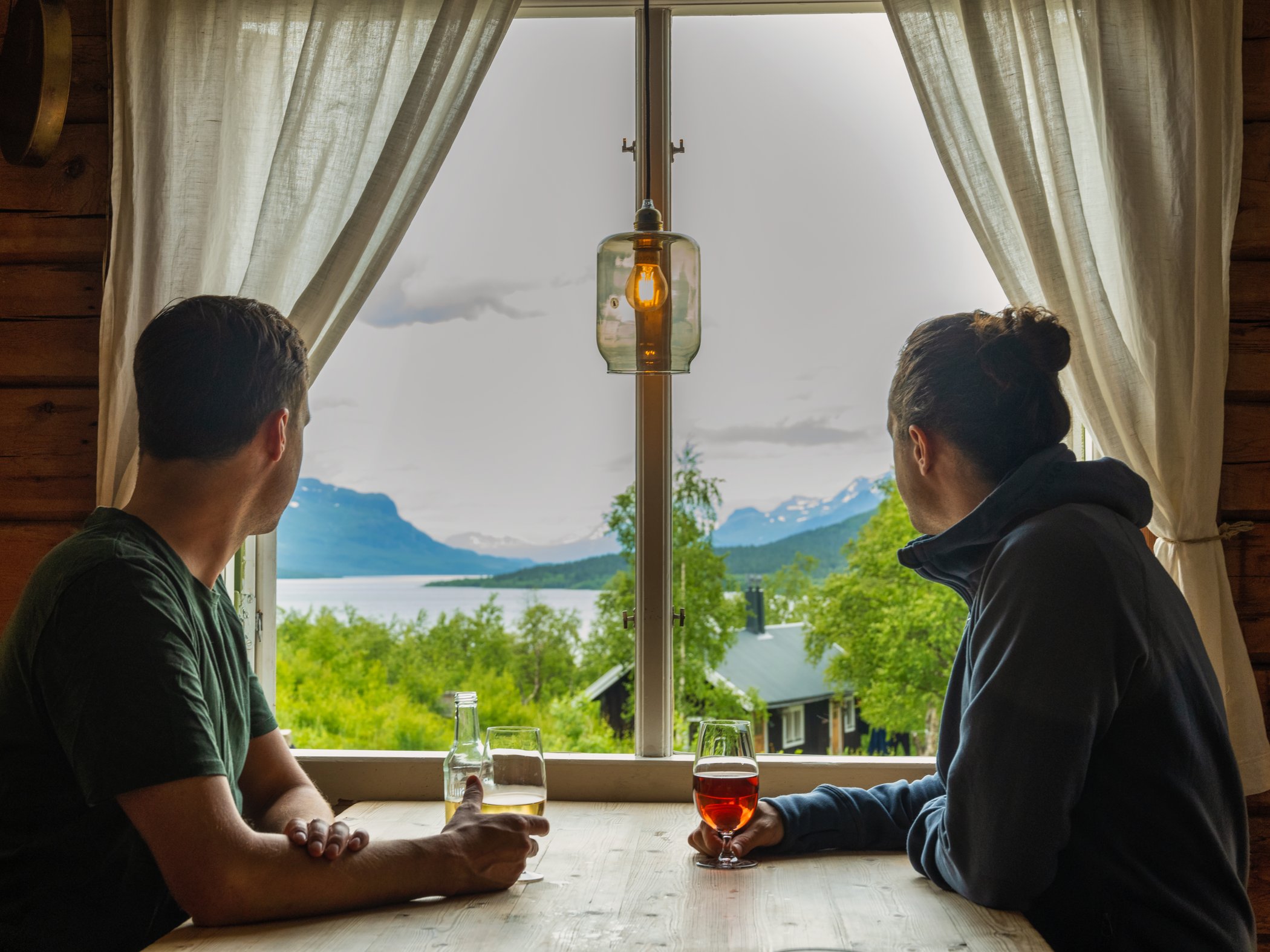 Två gäster sitter vid fönster och blickar ut över sjö och fjällandskap.