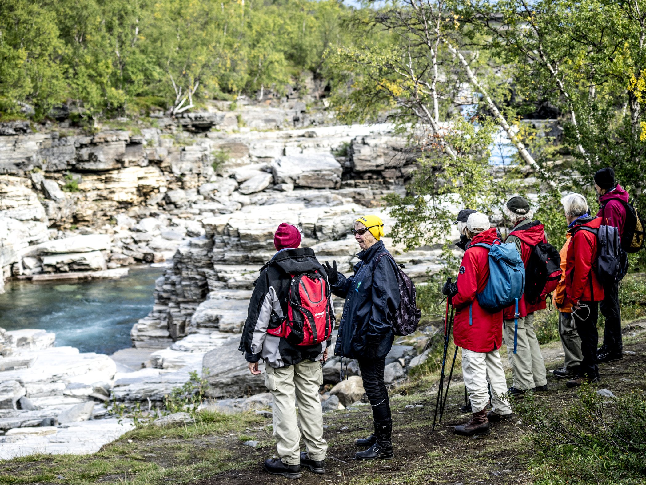Grupp vandrare står vid forsande vatten i fjällmiljö.