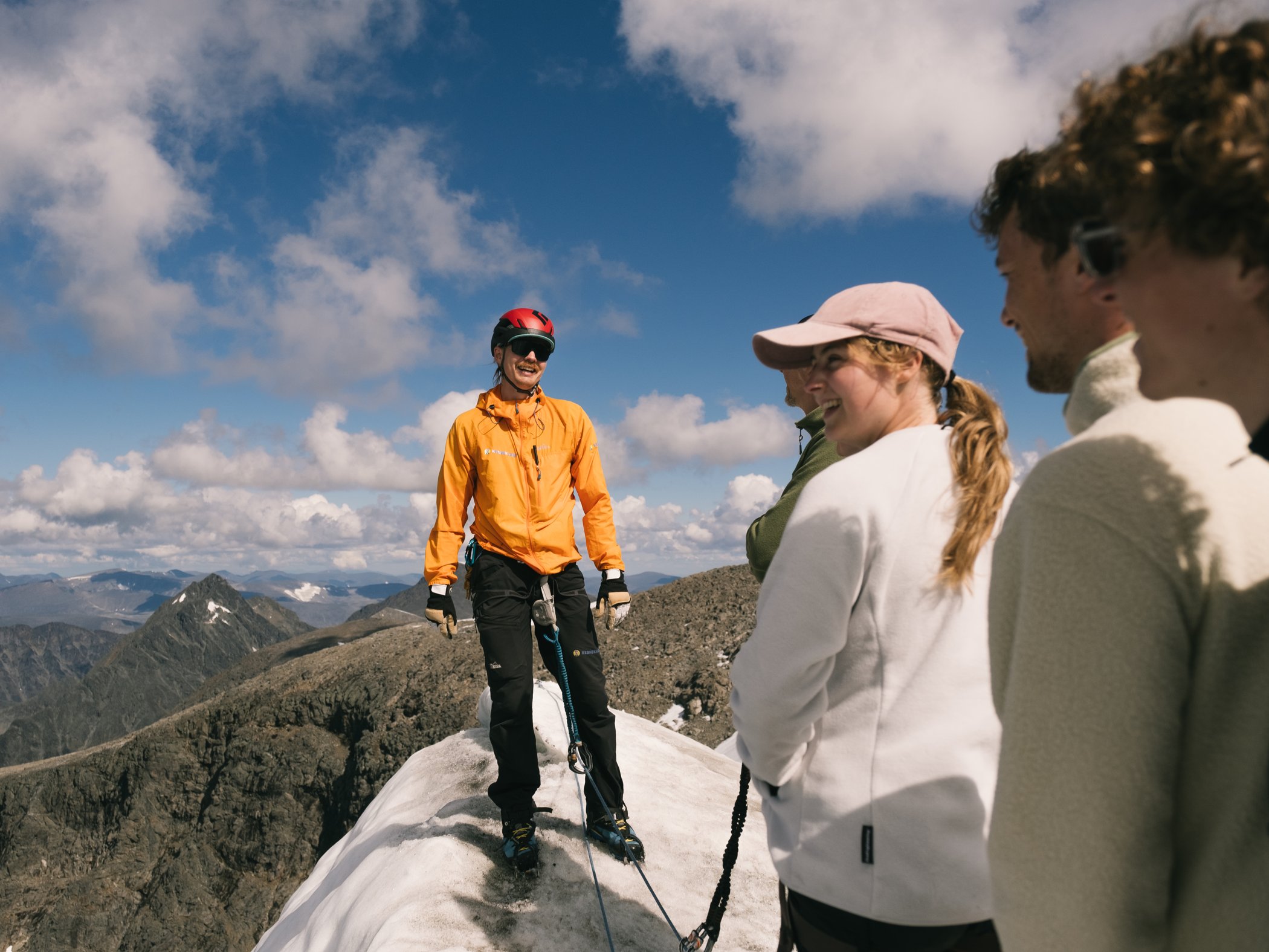 Guide står på snötäckt fjälltopp tillsammans med deltagare.