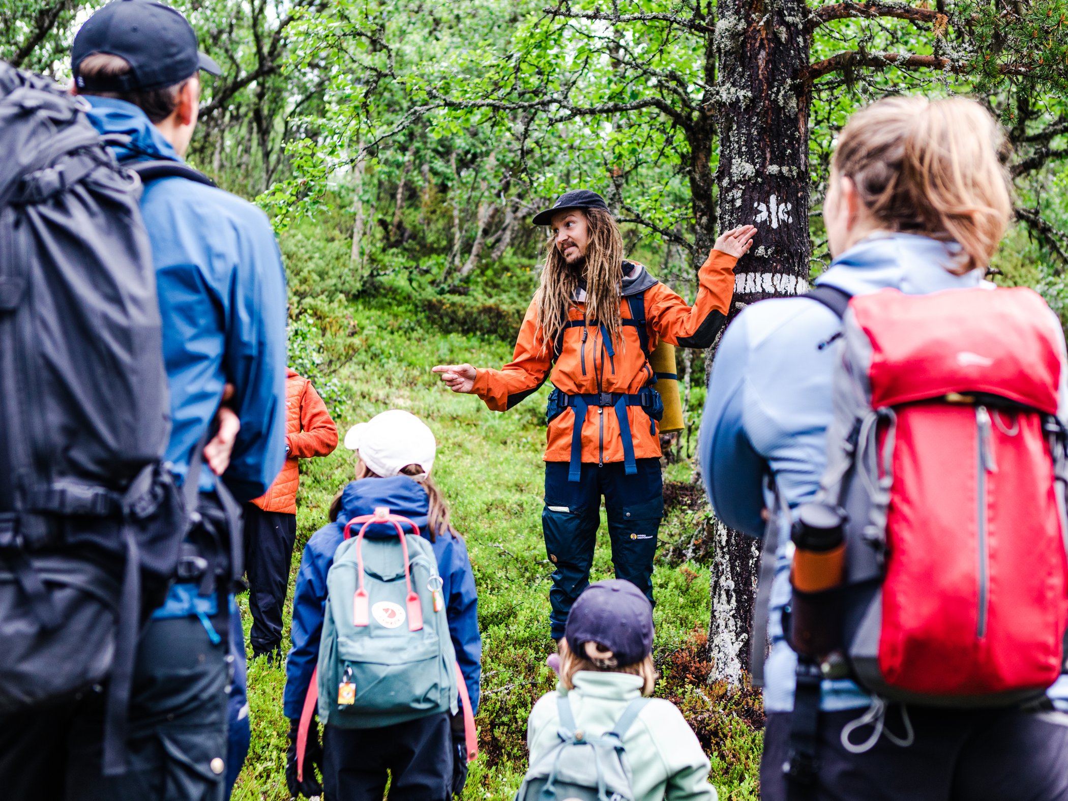 Guide visar ledmarkering för en grupp vandrare i fjällskog.
