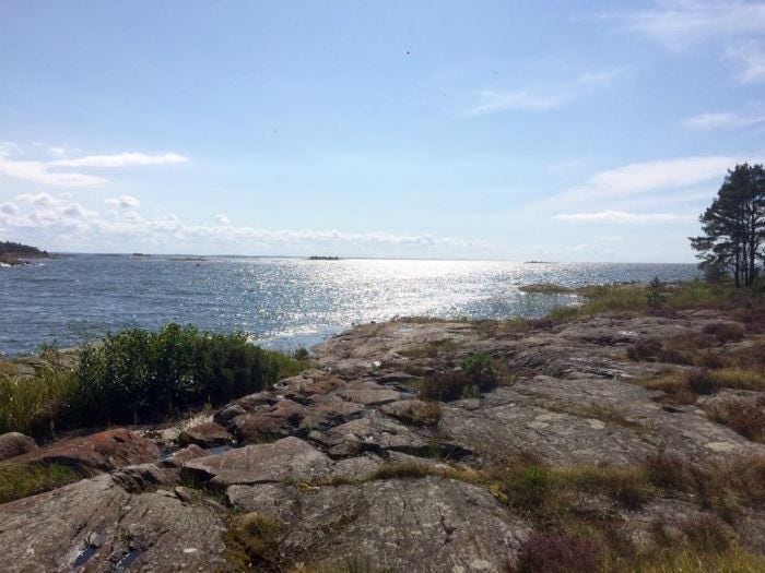 Klippig kust med utsikt över havet och skärgårdslandskap i solsken.