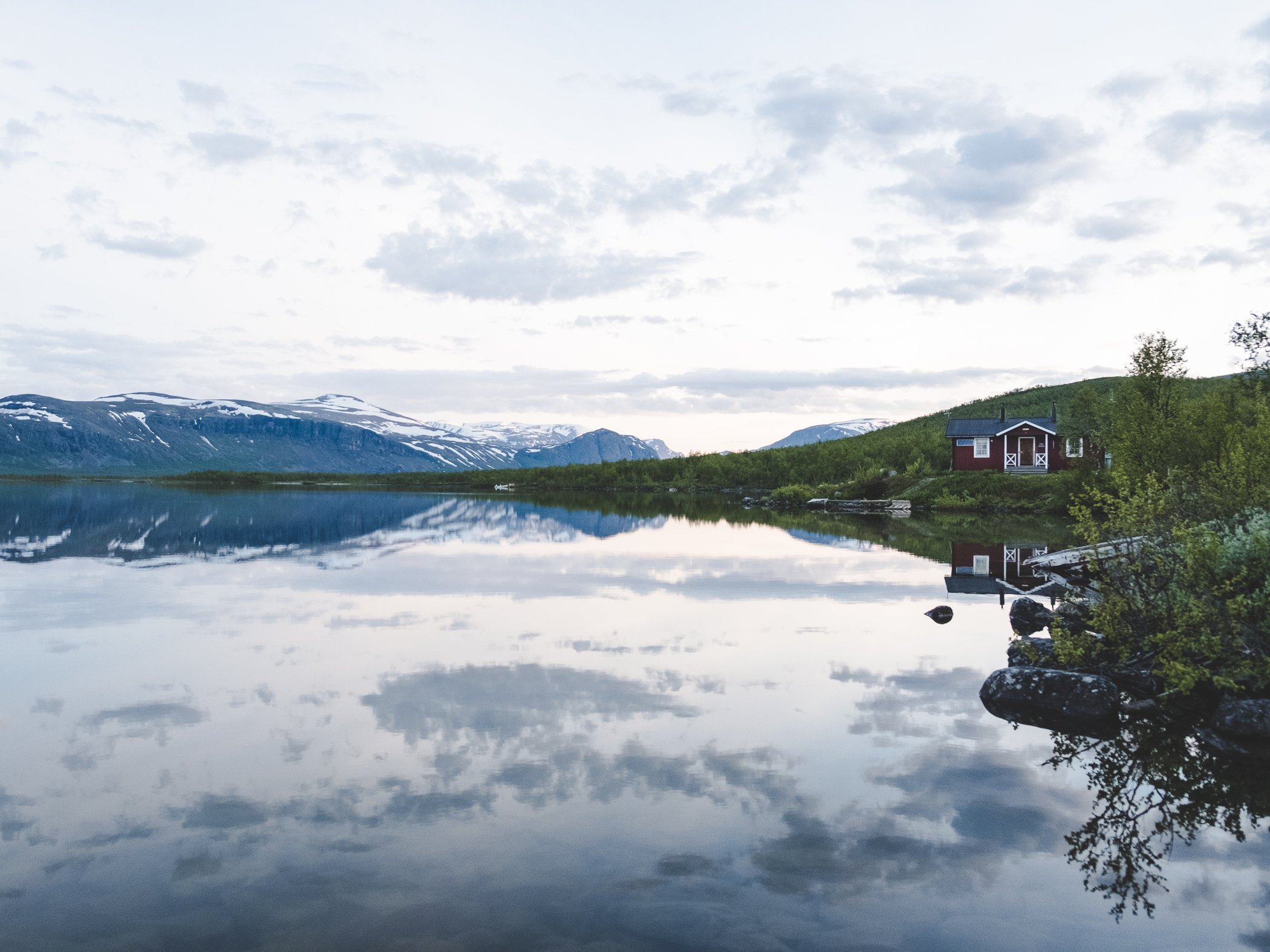 En stilla fjällsjö och en liten röd stuga.