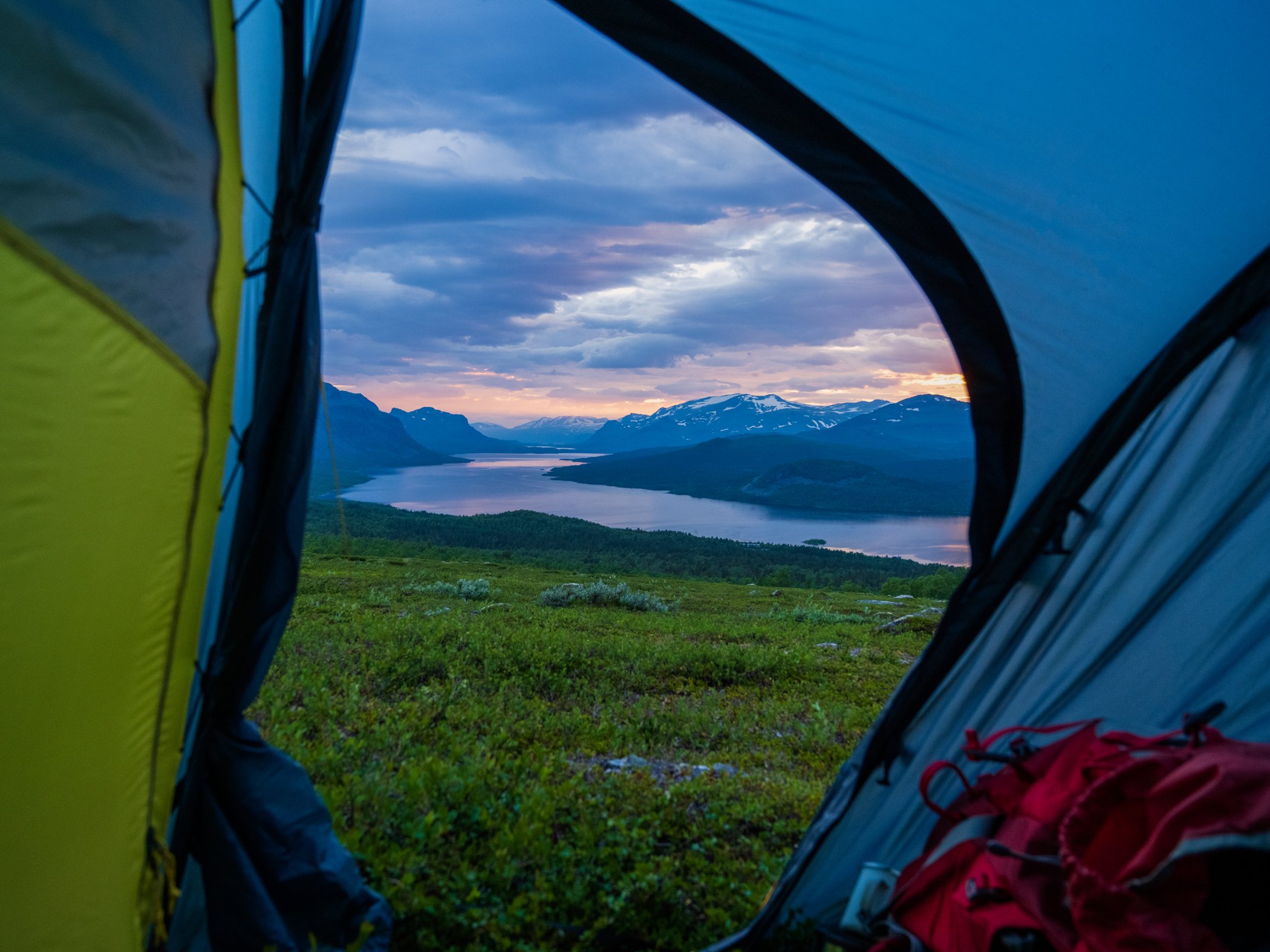 Utsikt över sjö och fjäll genom öppningen i ett tält i kvällsljus.