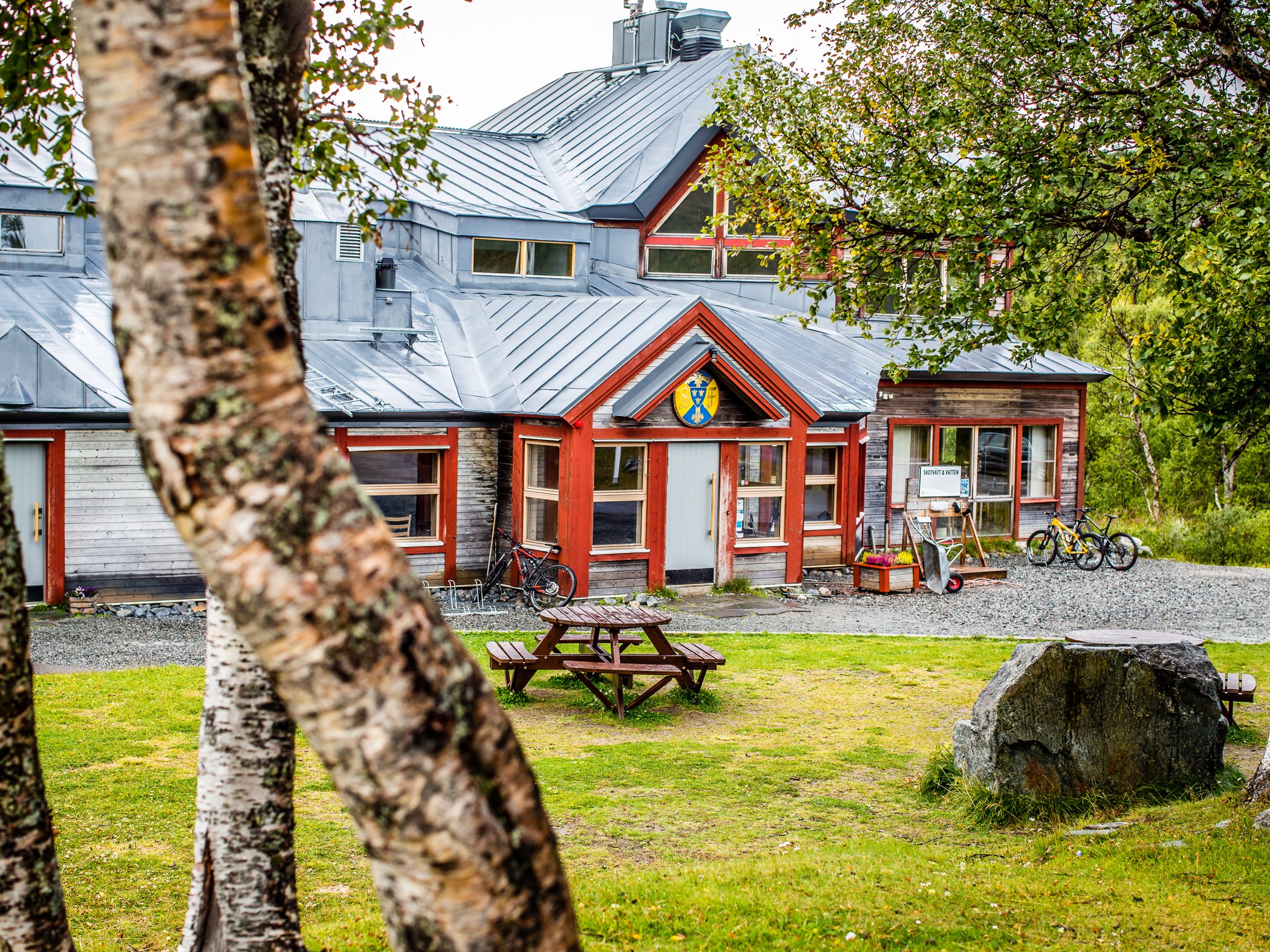 Fjällstation omgiven av björkar och grönska.