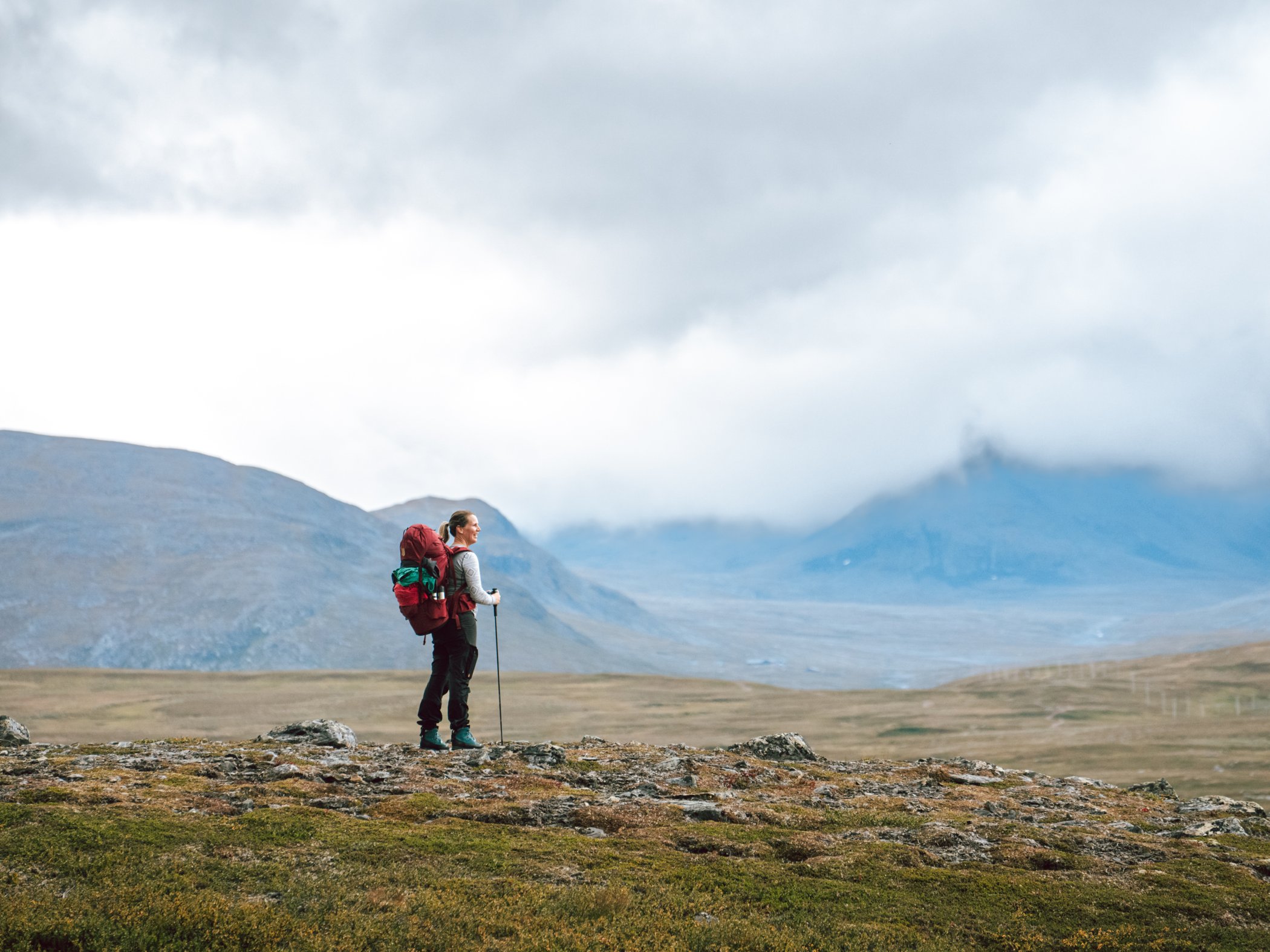Vandrare med stor ryggsäck på kalfjäll under molnig himmel.