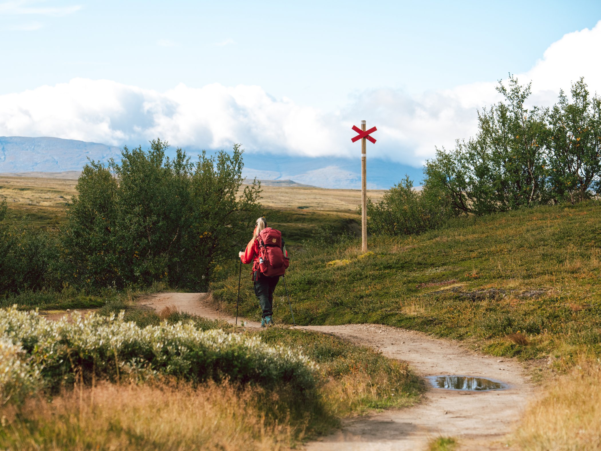Vandrare på fjällstig med röda ledkryss i landskapet.