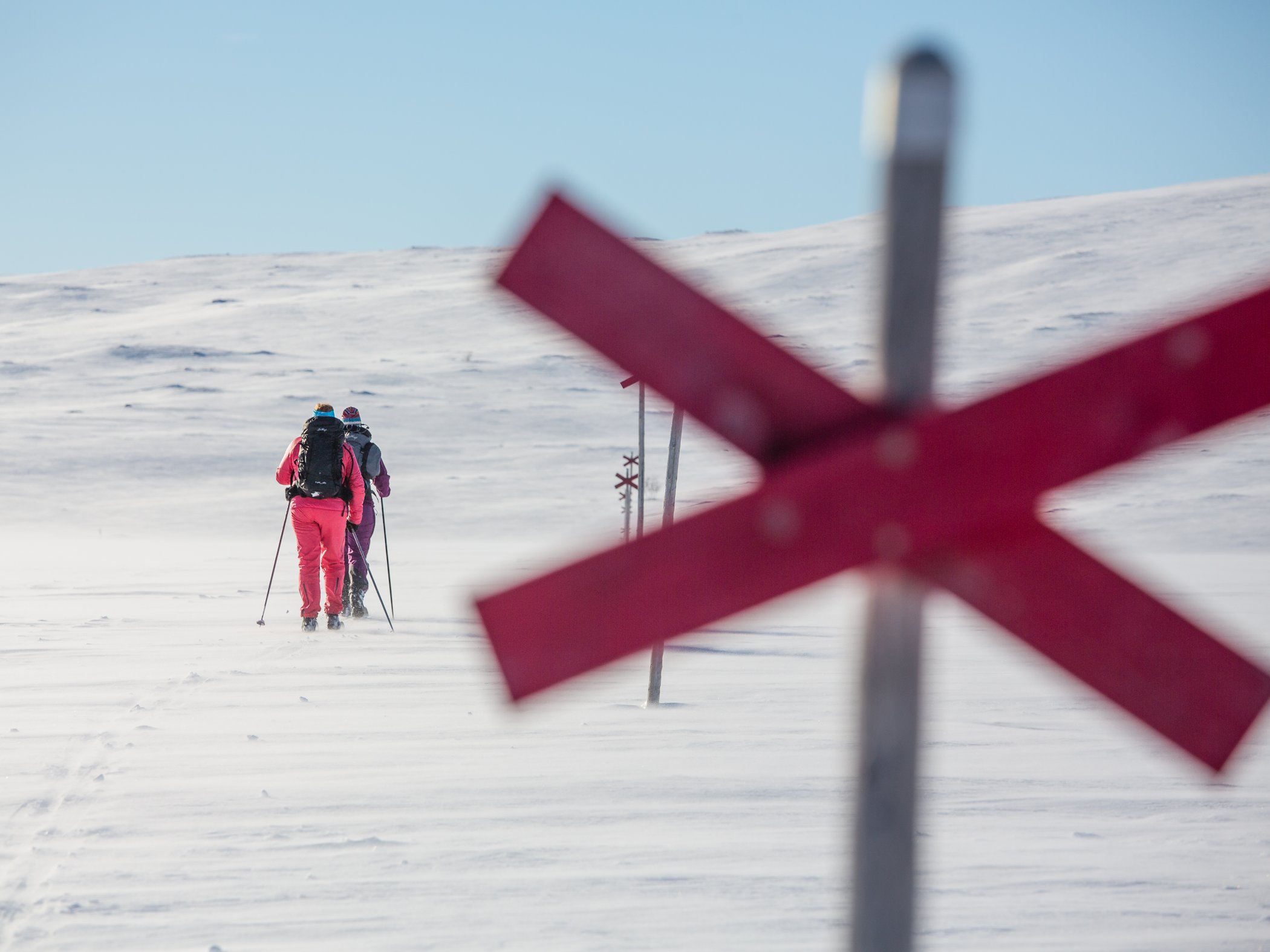 Två skidåkare som skidar utmed en kryssled i vintertäckt fjäll.