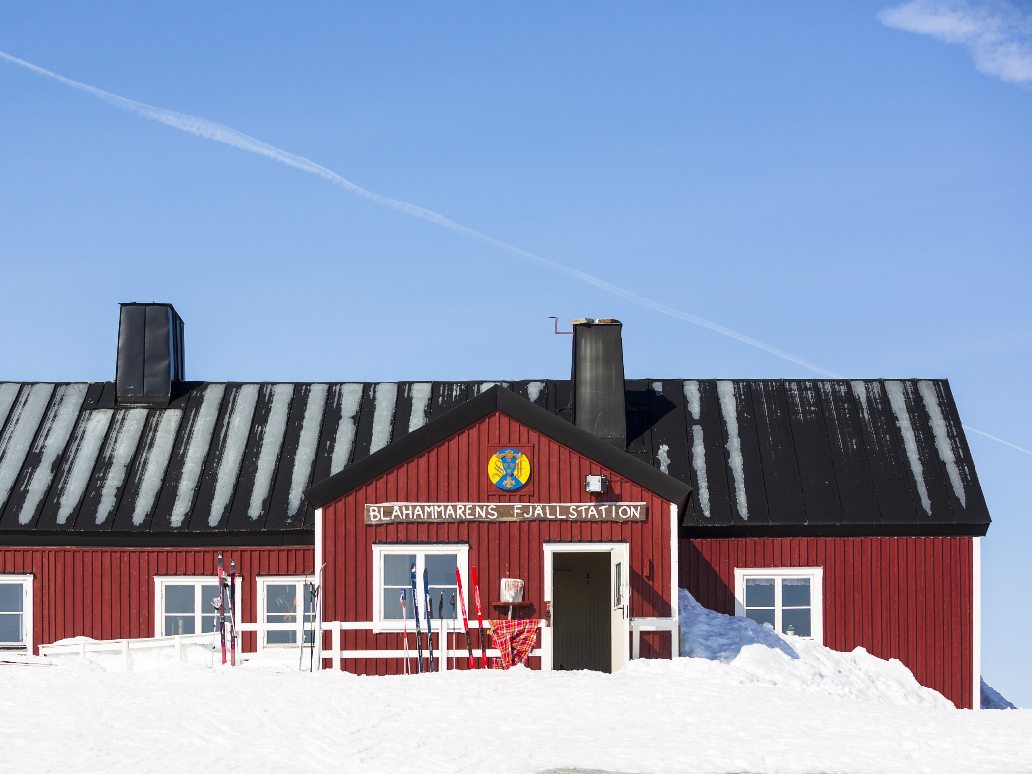 Ett rött hus med svart tak och blå himmel.