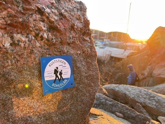 Markering för Kuststigen på klippa i Bohuslän med skärgårdsmiljö i kvällsljus.