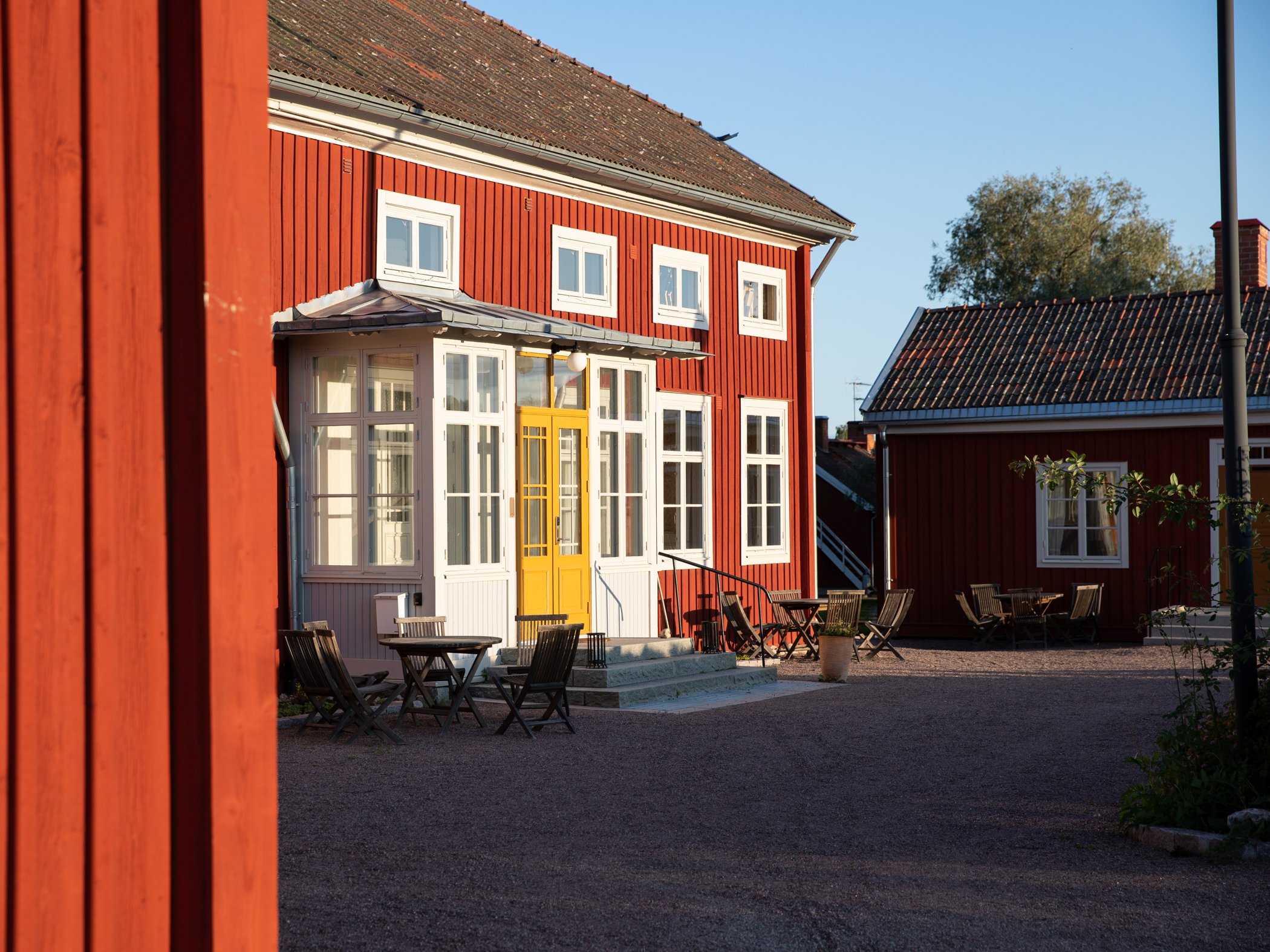 Röda trähus med gula detaljer och uteservering i kvällssol.