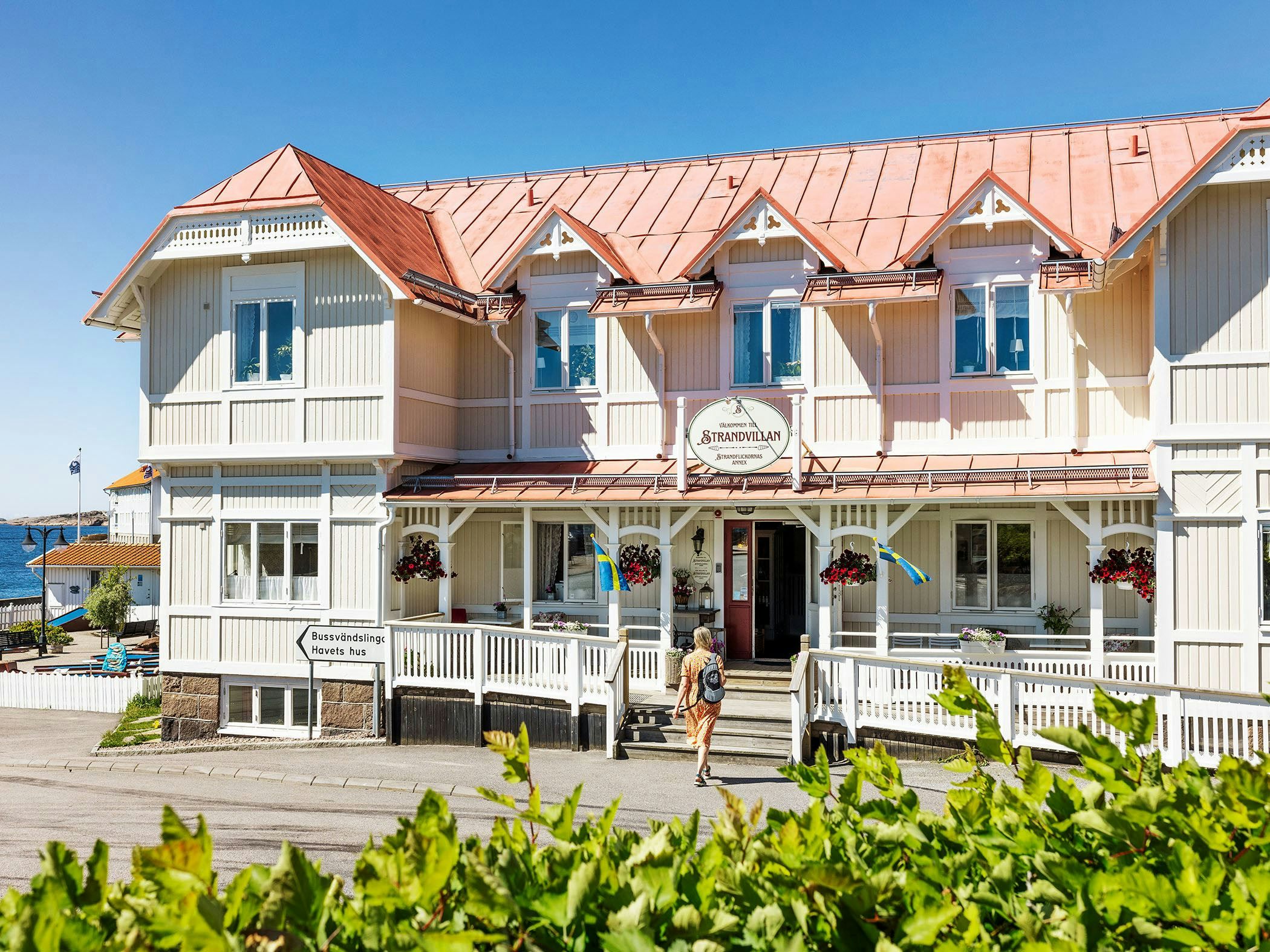 Strandvillan i skärgårdsmiljö med vit träfasad, blomsterprydd entré och havet i bakgrunden.