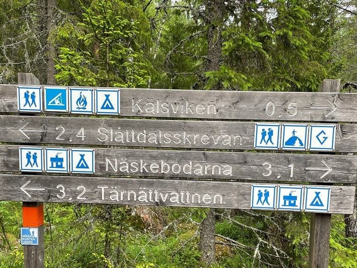 Vägvisare med information om vandringsleder, rastplatser och tältplatser i skogslandskap.