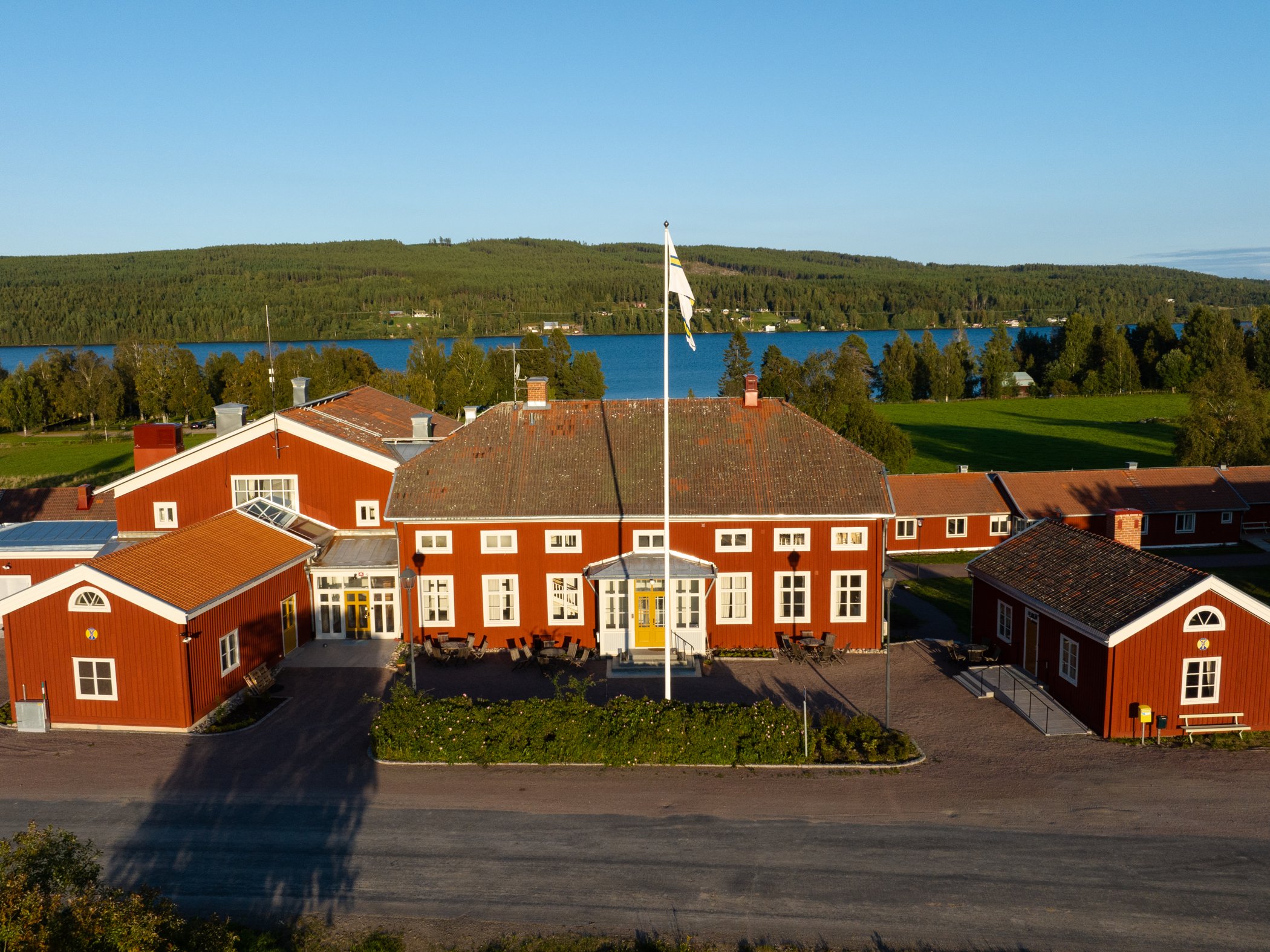Röd herrgårdsbyggnad med gula detaljer vid sjö och grönskande landskap.