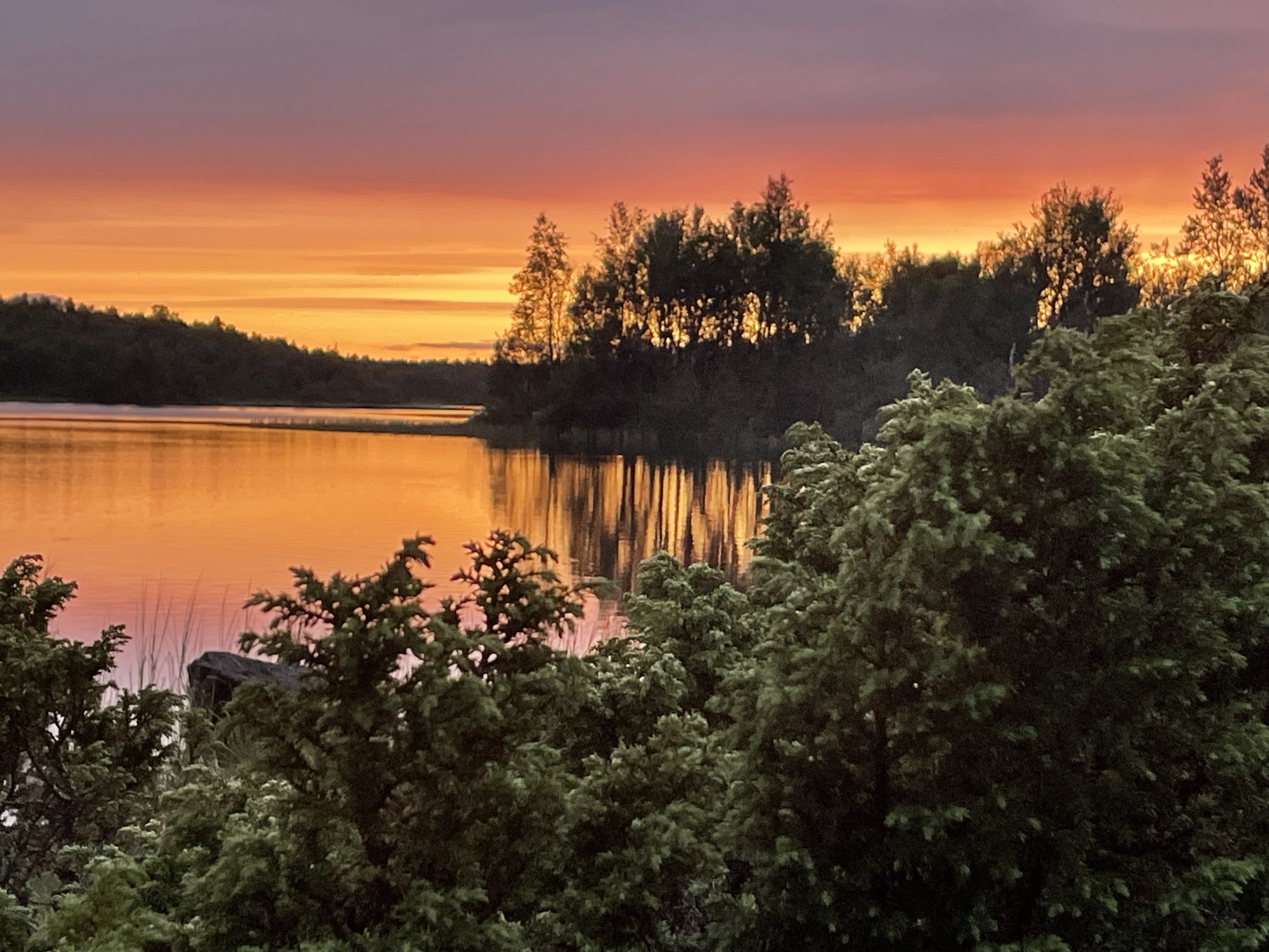 Solnedgång i rödorange över stilla sjö.