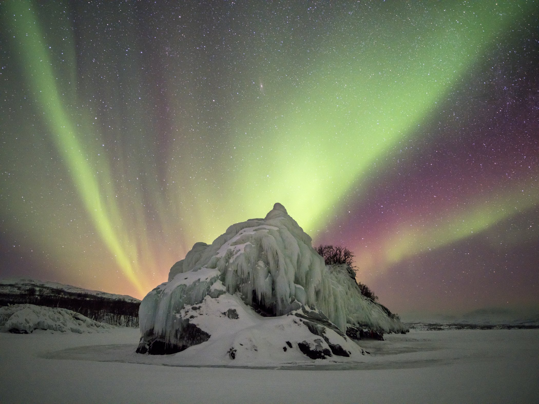 Frusen isformation upplyst av färgstarkt norrsken under en klar vinternatt i Abisko.