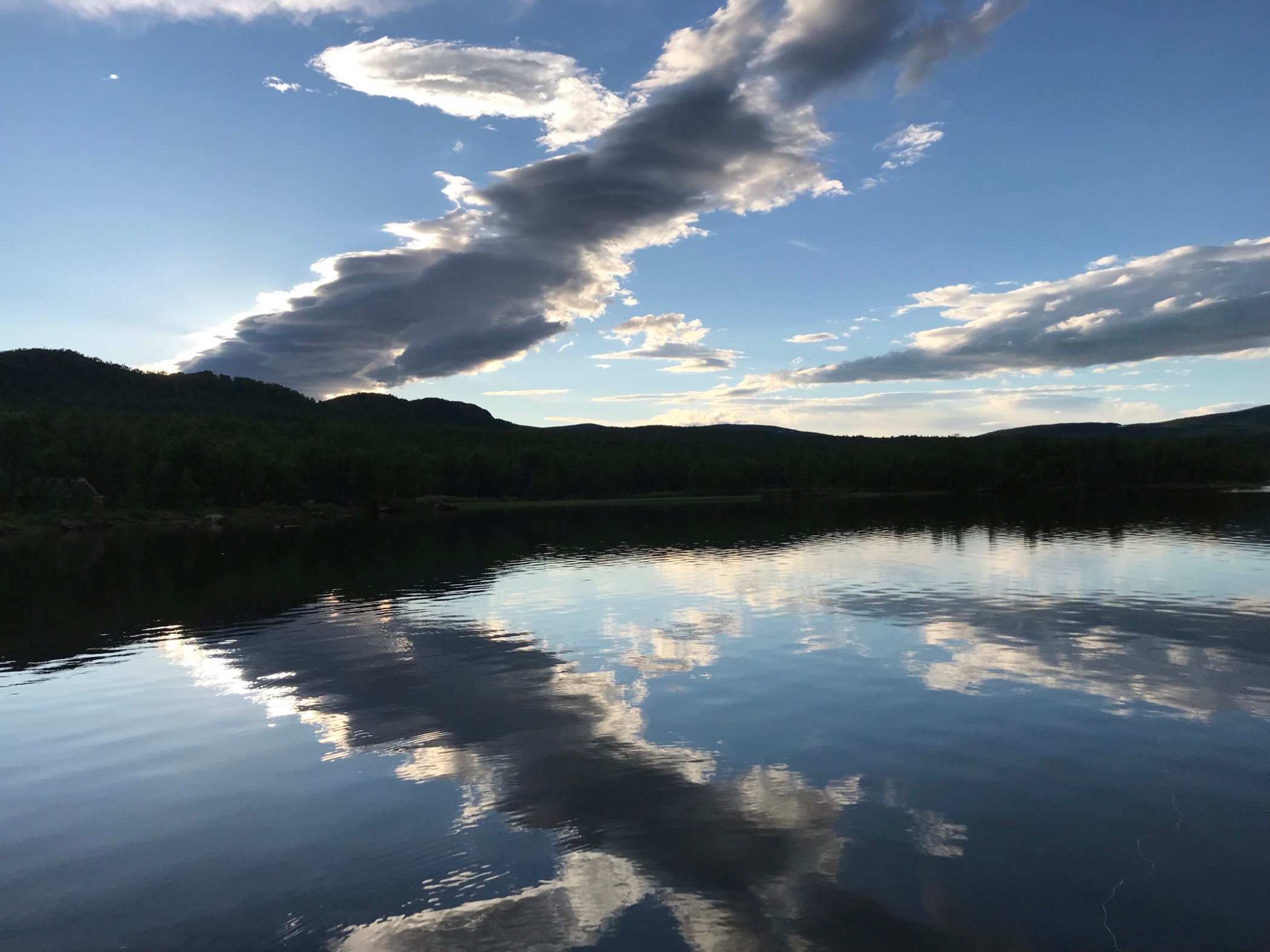 En fiskesjö i solsken med vackra moln på himlen. 