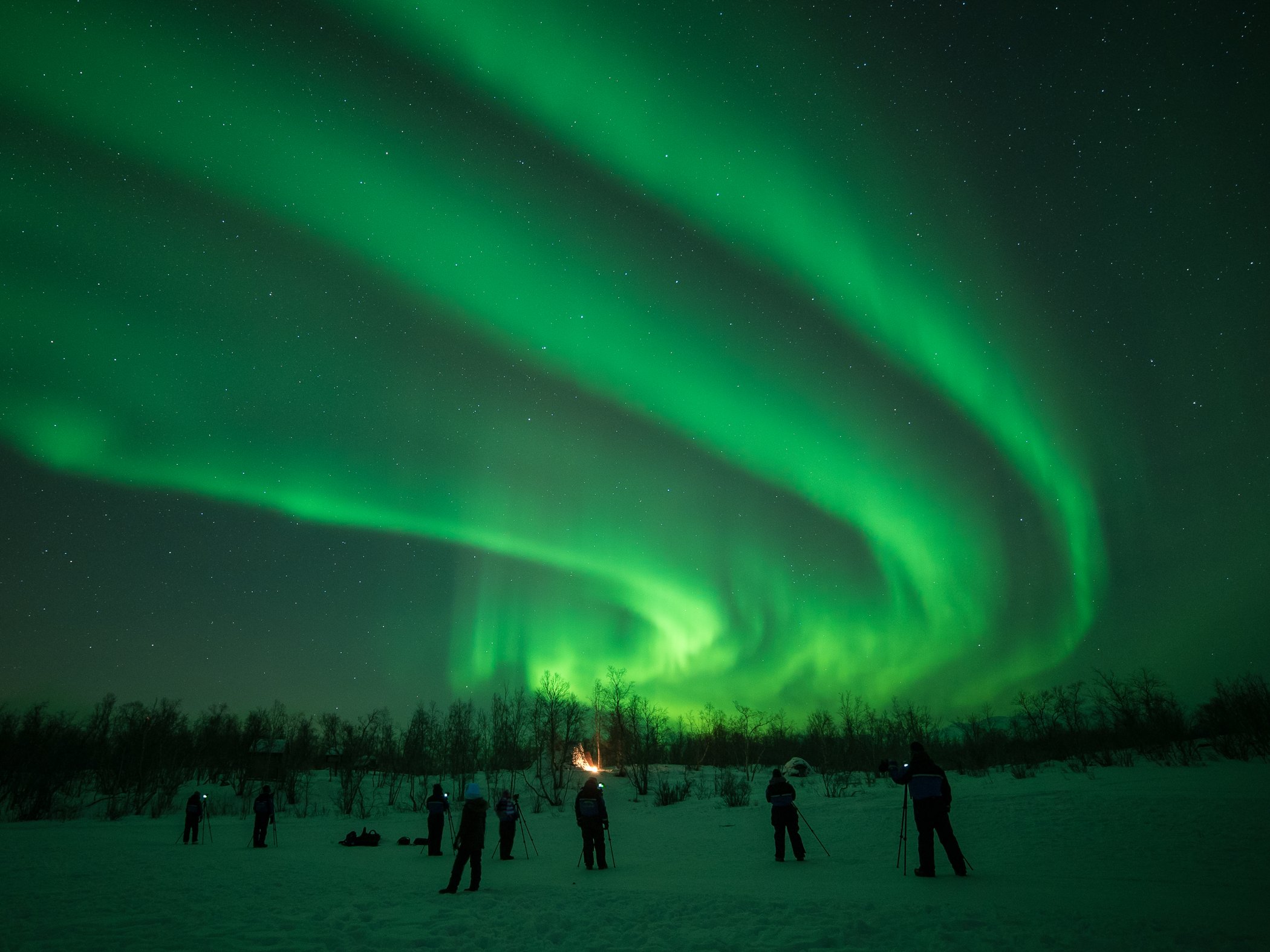 Besökare fotograferar norrsken över ett snötäckt landskap i Abisko.