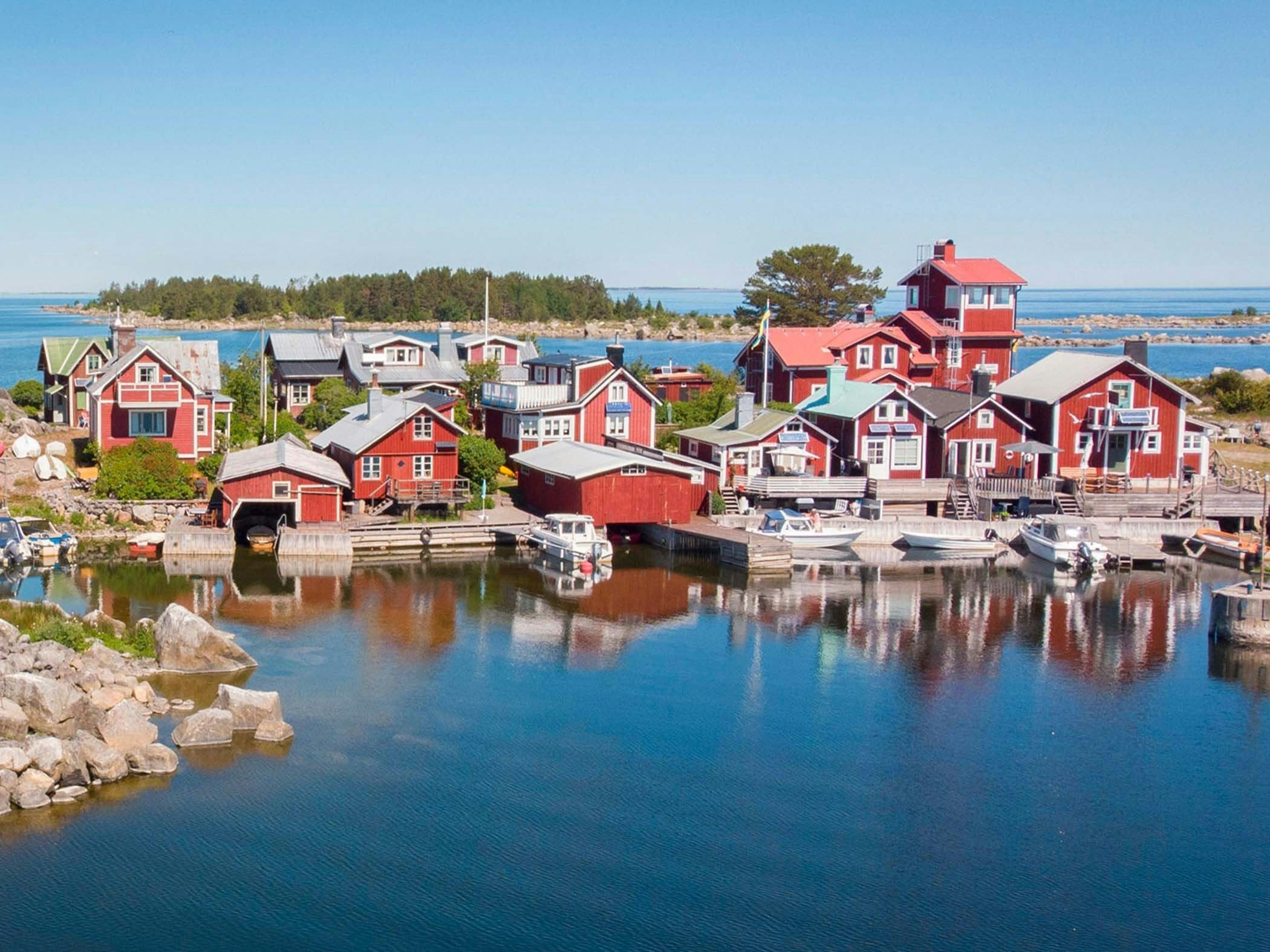 Fiskeläge med röda sjöbodar, småbåtshamn och skärgårdsvatten under en klar sommardag.