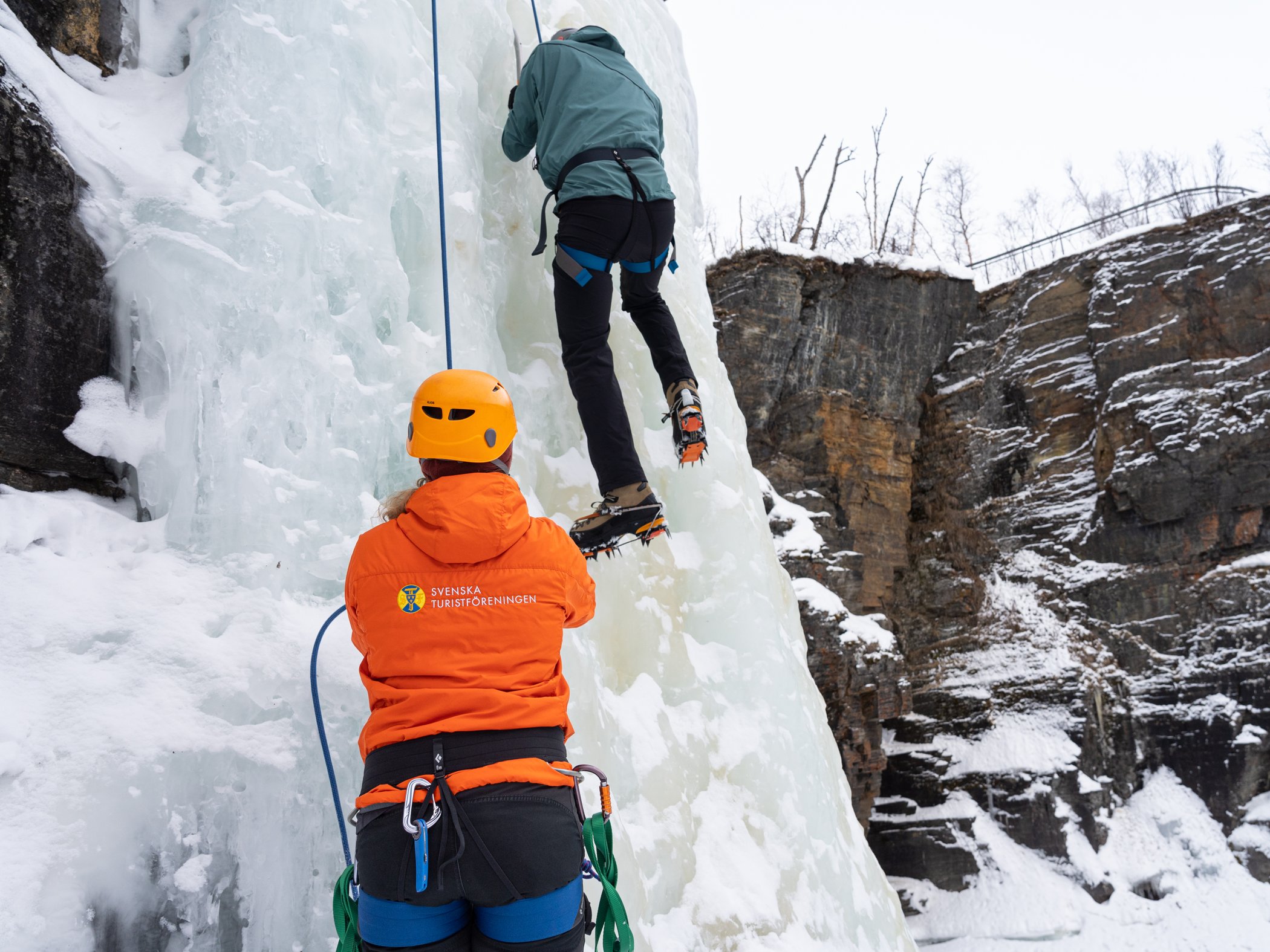 Guide säkrar en klättrare på en frusen isvägg under isklättring i Abisko.
