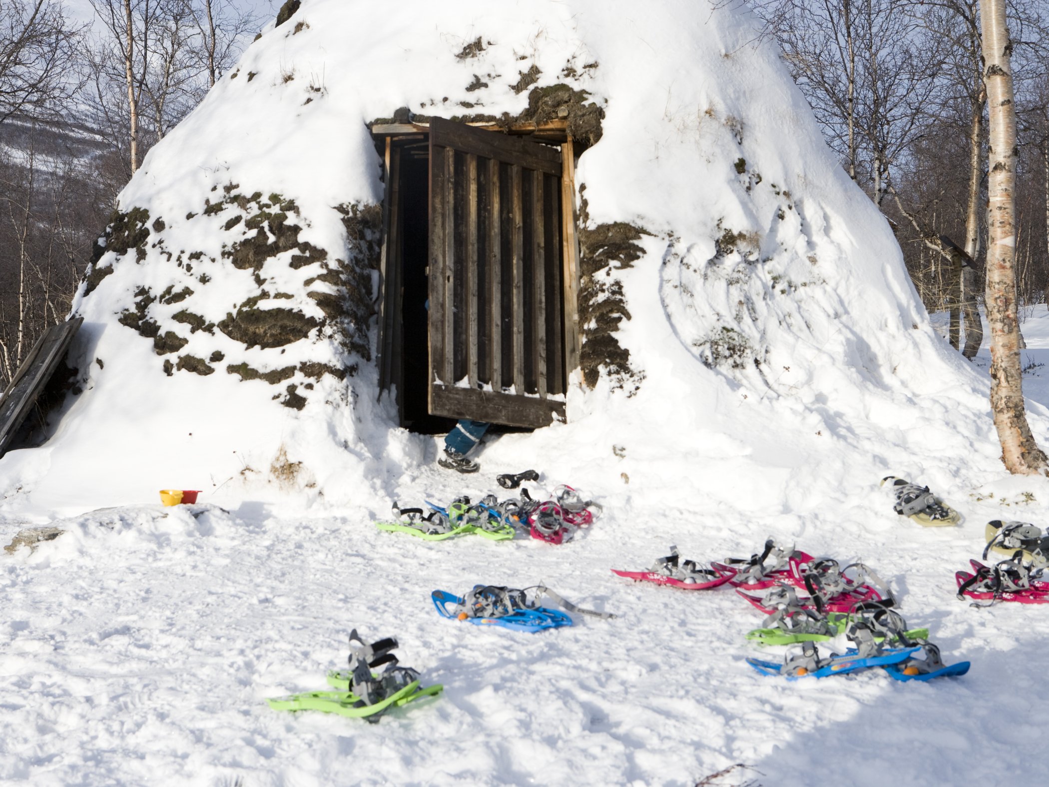 Snöskor ligger utanför en snötäckt snögrotta i vinterlandskap.