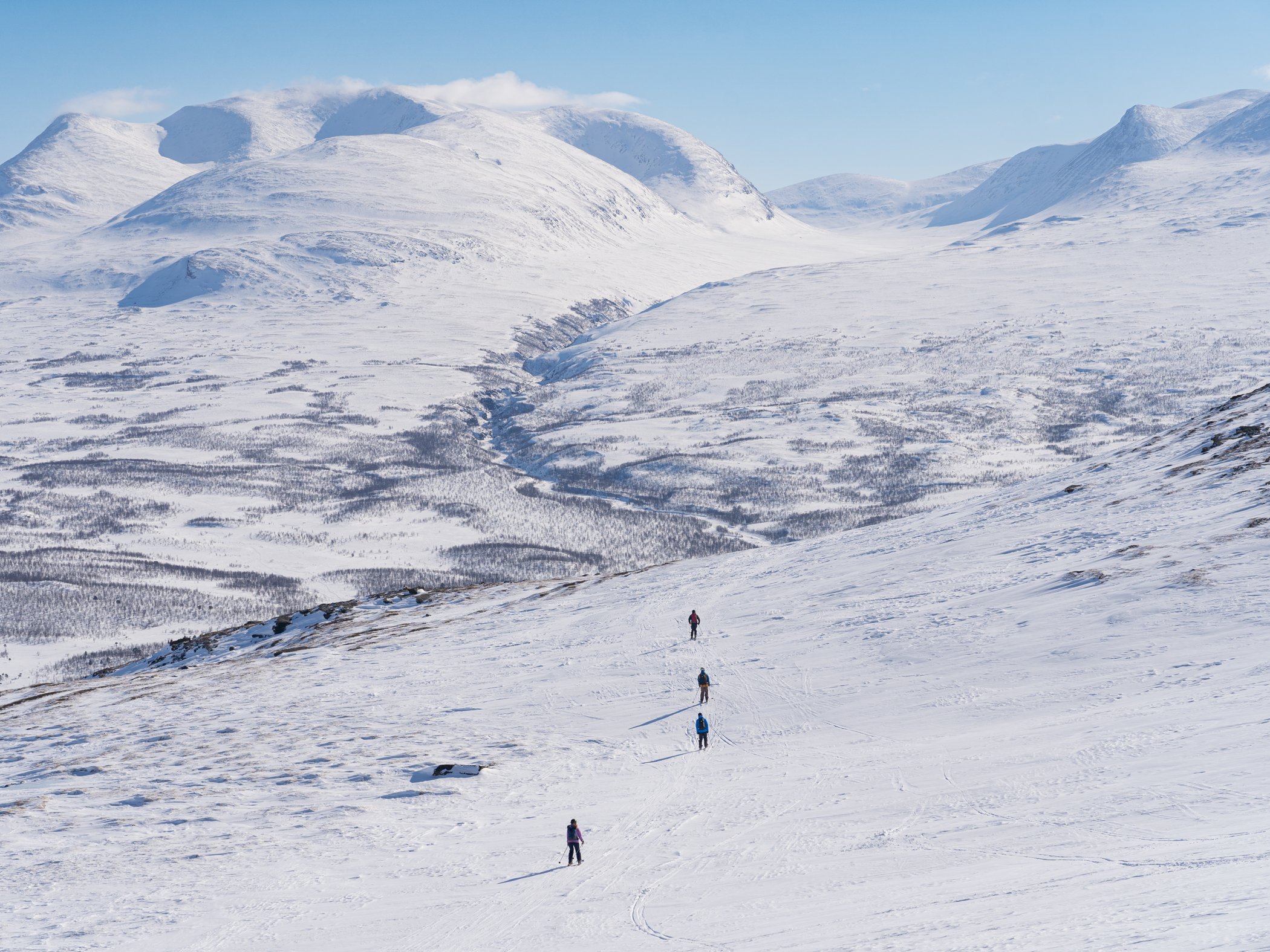 Skidåkare färdas genom det öppna fjällandskapet under en topptur i Abisko.
