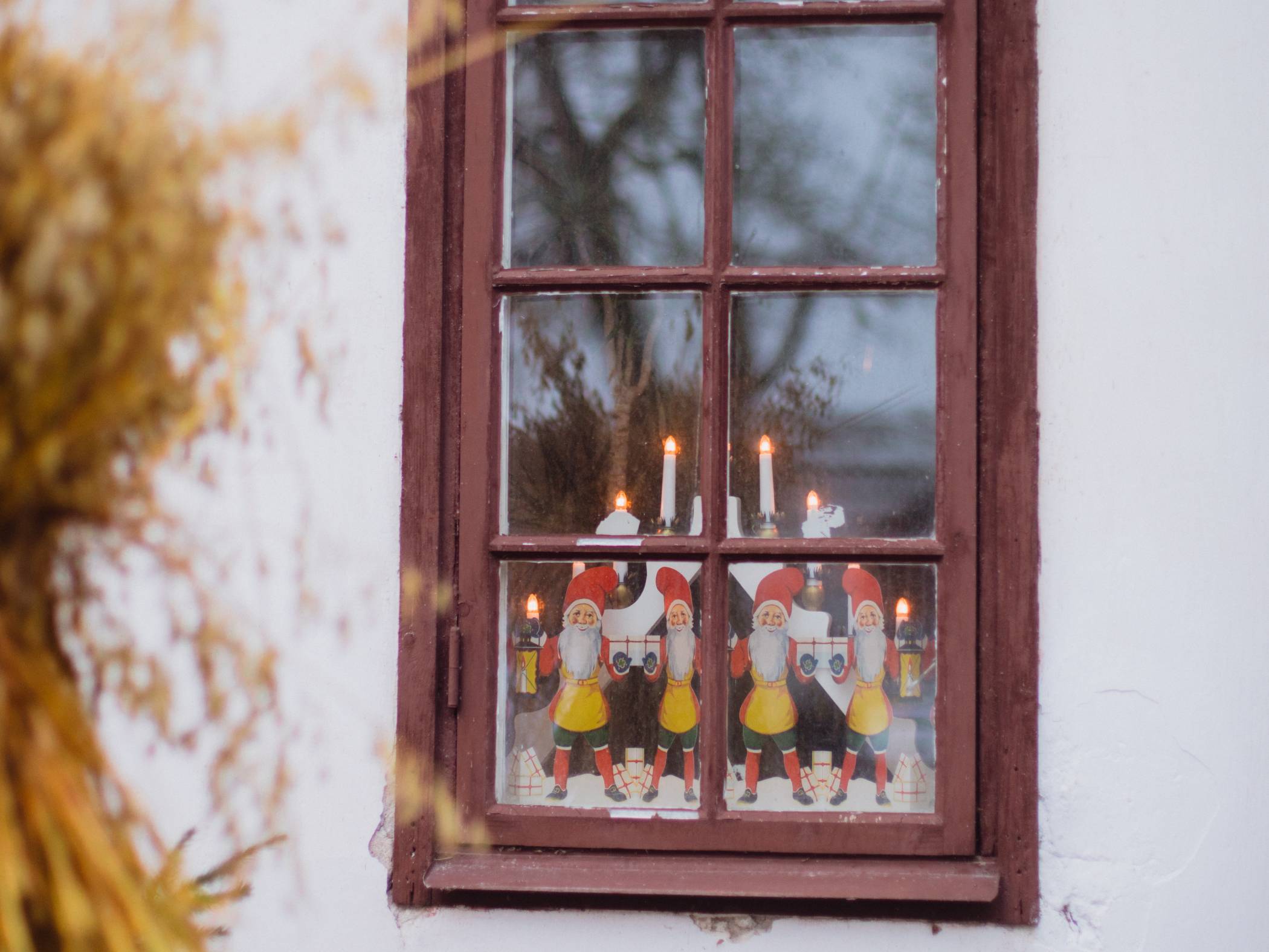Bild på ett fönster utifrån under vintern som är dekorerat med julpynt som tomtar och adventsljusstake.
